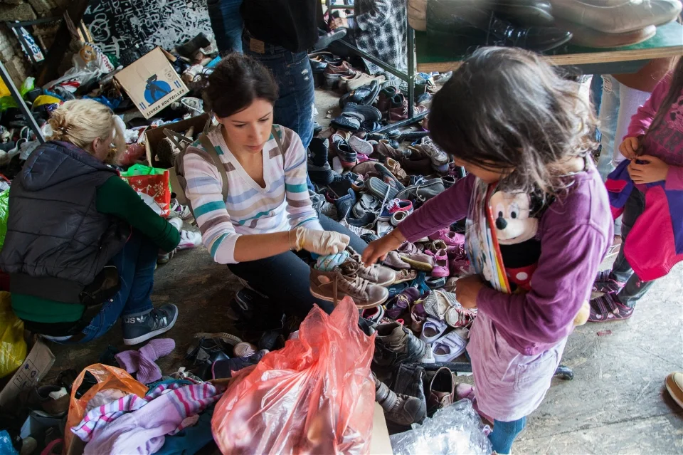 A volunteer helps a young Syrian girl find new shoes and socks at Miksaliste, a hub for the refugee response in Belgrade (James Haines-Young/IRIN)