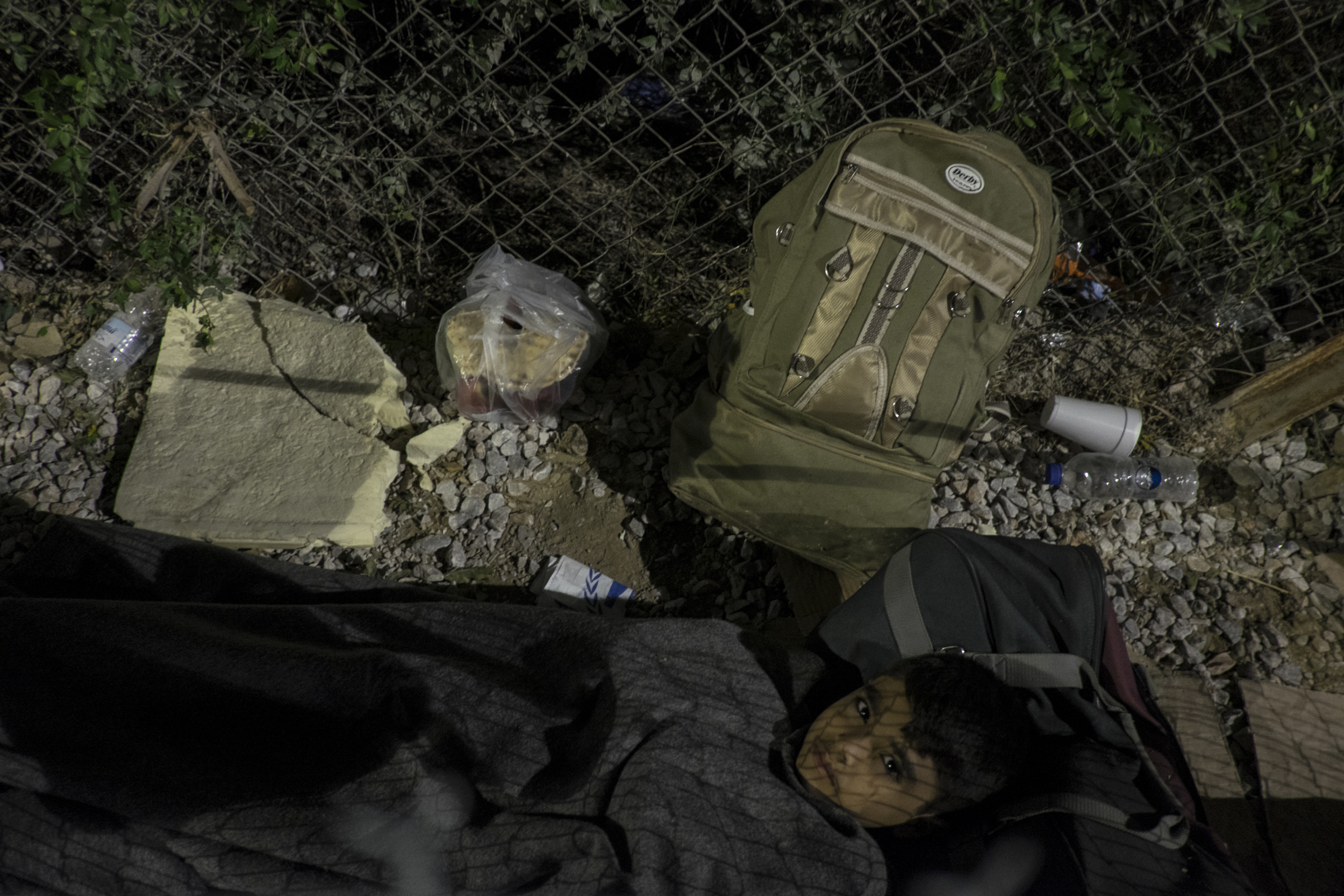   A boy, who is by himself, tries to sleep on a piece of cardboard next to the fence outside Moria reception centre  