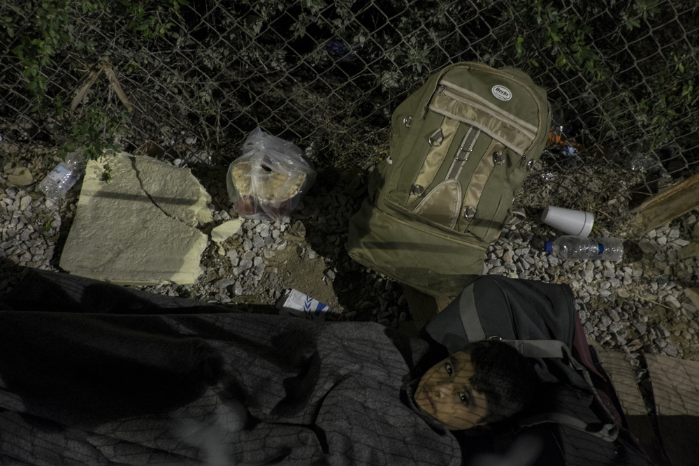   Seul, ce jeune garçon tente de dormir sur un bout de carton à l’extérieur du centre d’accueil de Moria, le long de la clôture  