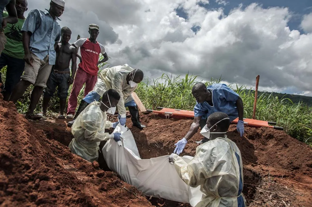 M. Momorie (debout dans la tombe à gauche) descend le corps d’une vieille femme dans un cimetière local