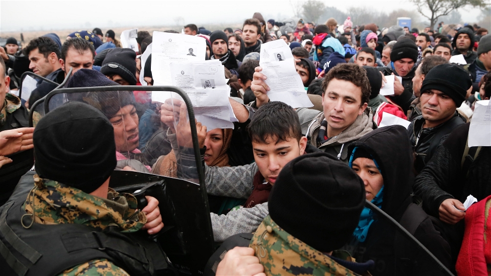 Migrants and refugees wave their Greek registration papers at the border with Macedonia where only certain nationalities were being allowed to cross (Dimitris Tosidis/IRIN) 