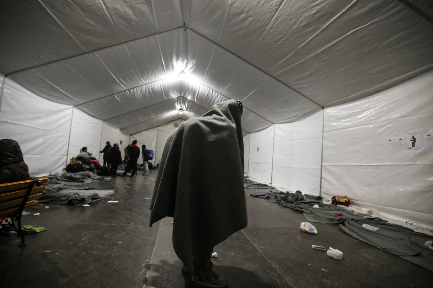 Une couverture sur le sac à dos, un réfugié lutte contre le froid dans une tente chauffée du camp de transit d’Idomeni