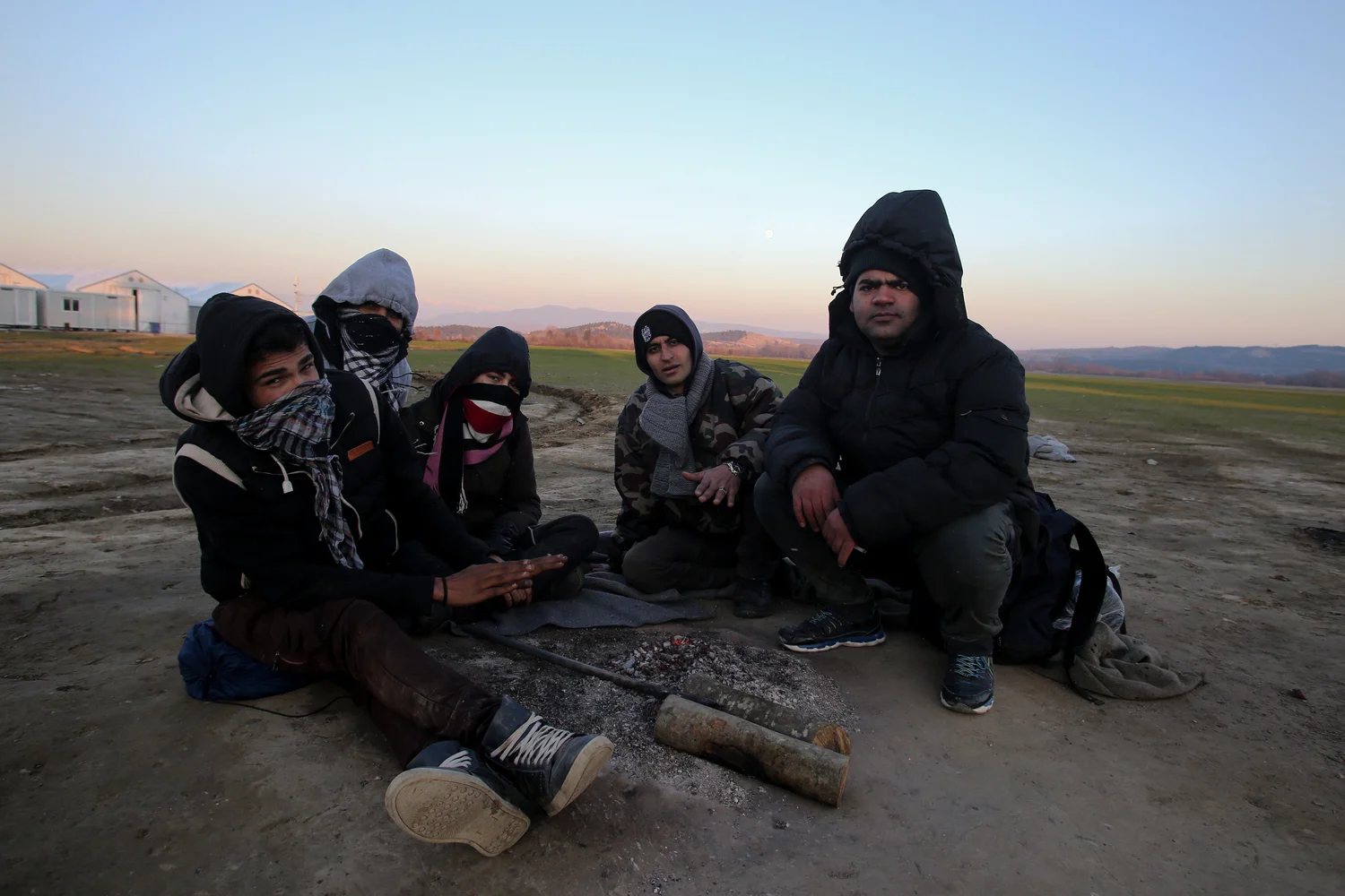 A group of young Iranian migrants who have been stranded at Greece's border with Macedonia for three days, try to keep warm around a small fire (Dimitris Tosidis/IRIN)