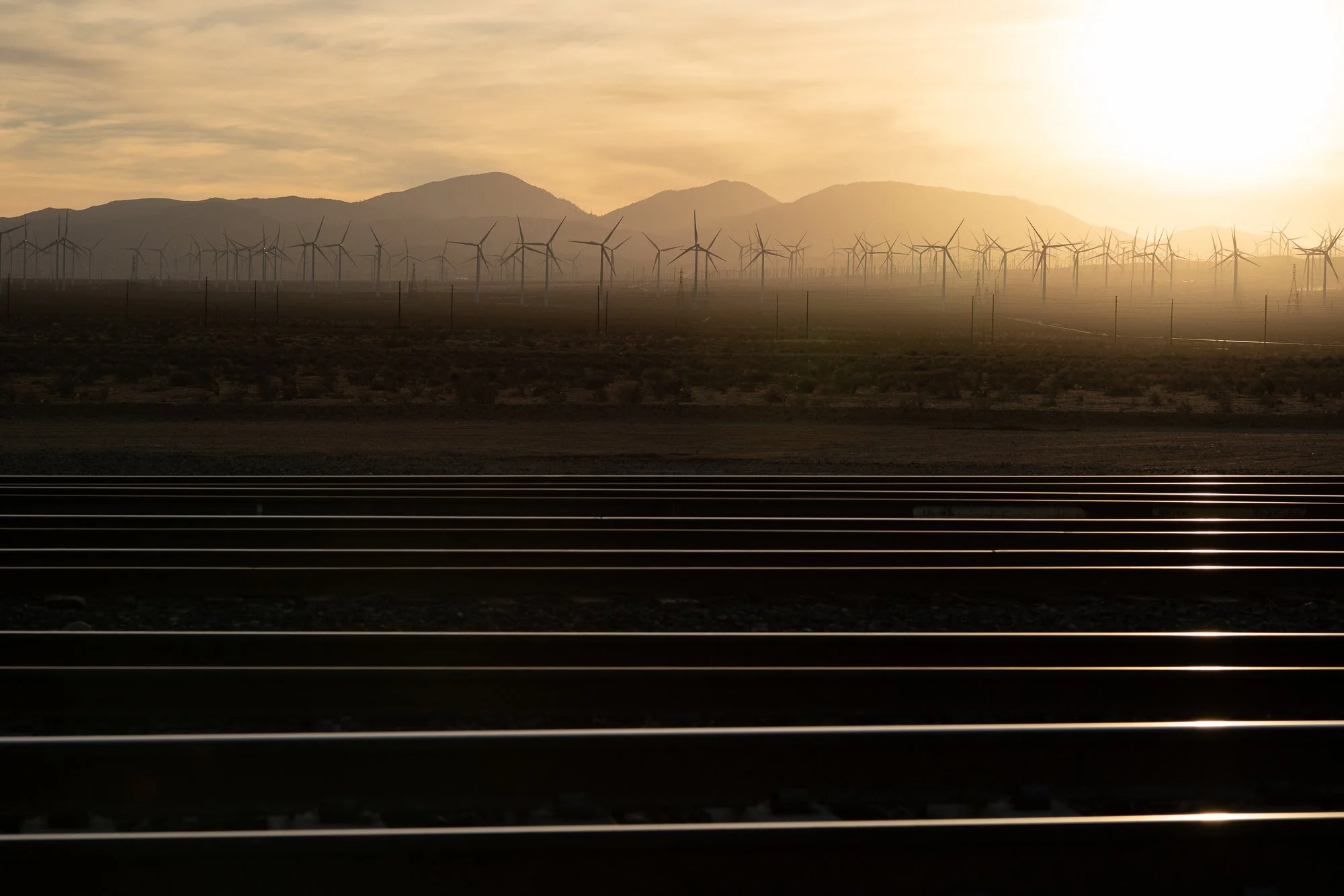 Railroad tracks and wind turbines across the California desert at sunset