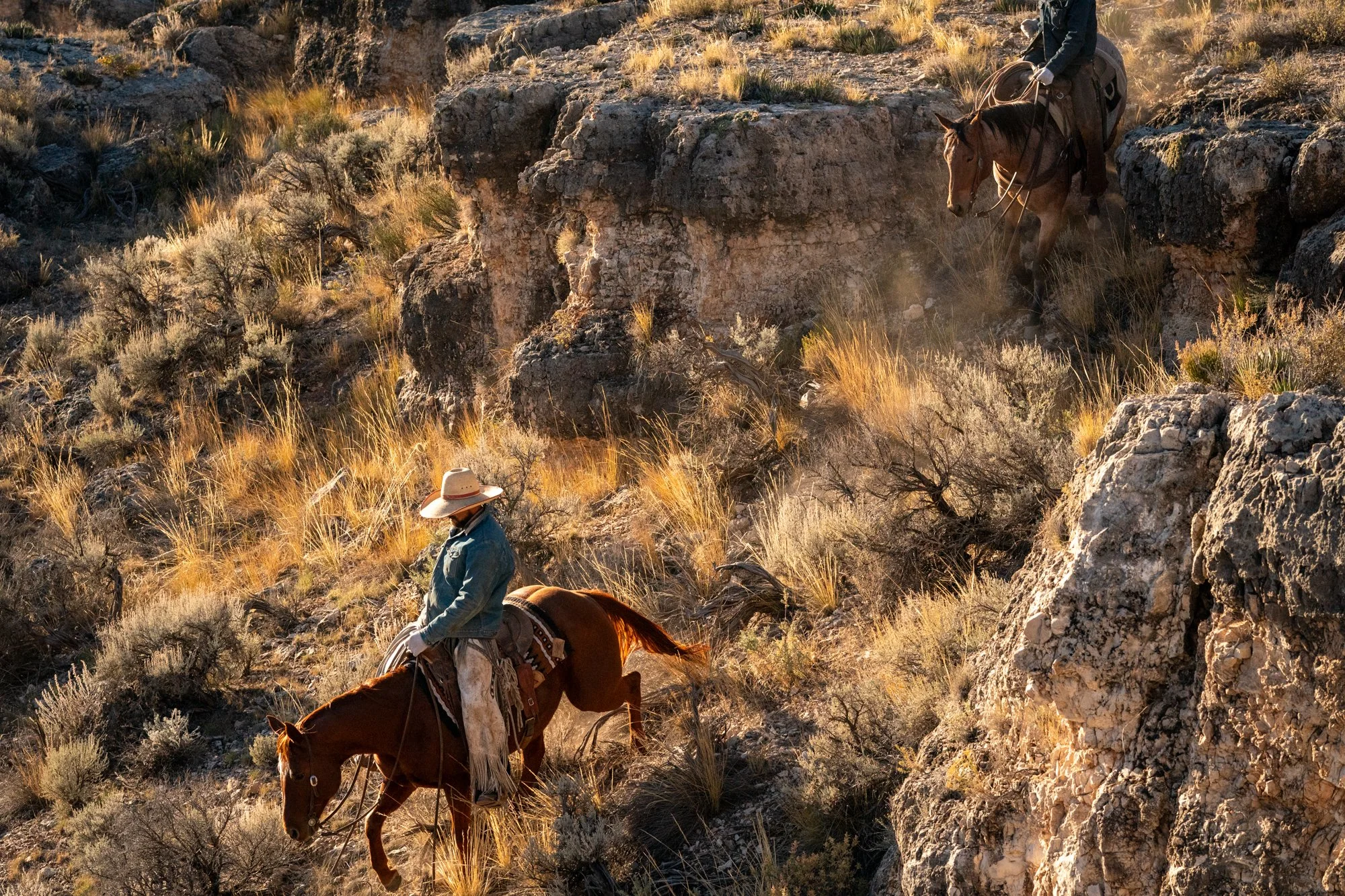 Cowboys riding horses through rough desert terrain on a working ranch