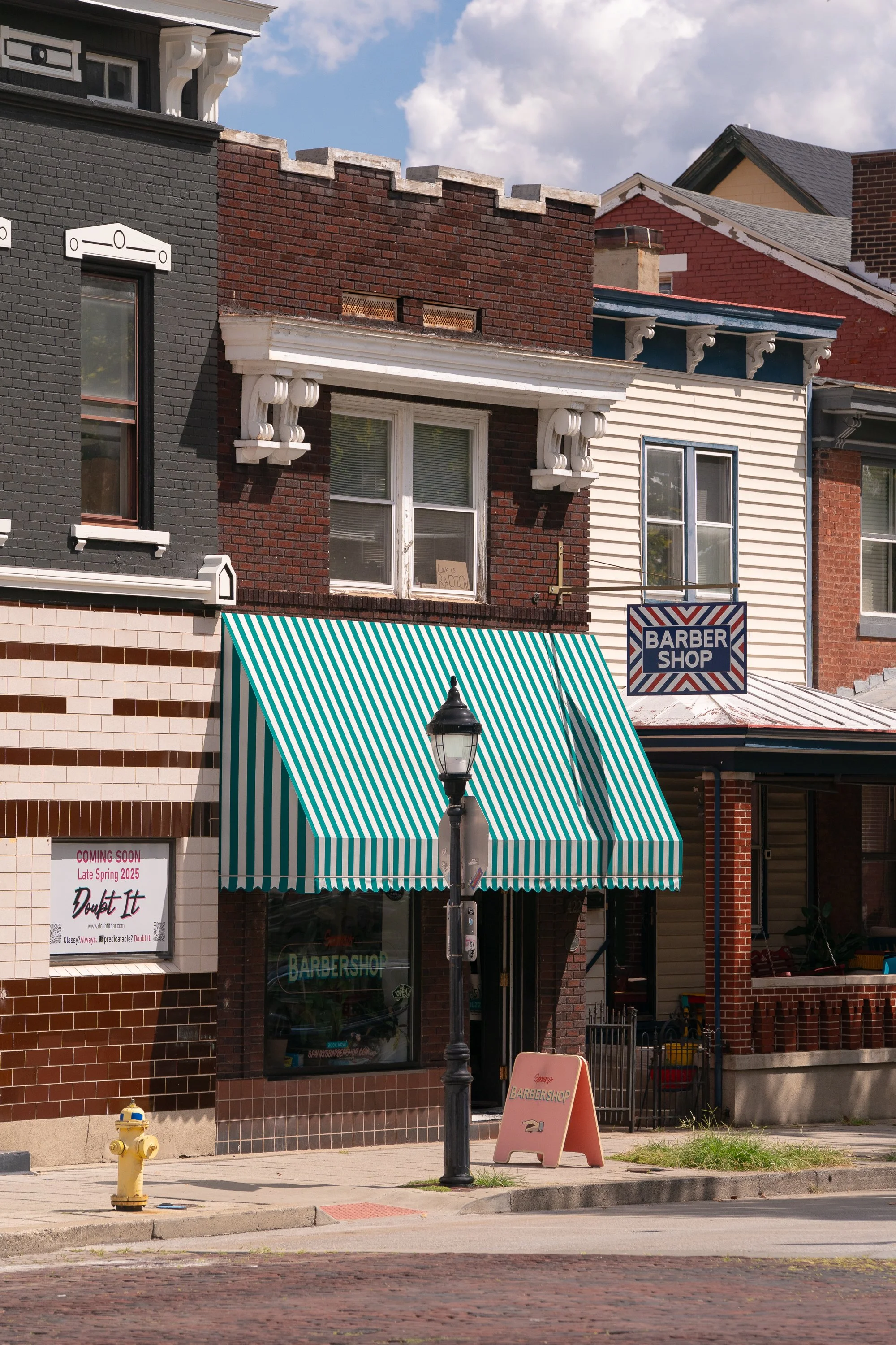 Exterior of Spanky’s Barbershop in Covington, Kentucky with green striped awning and brick storefront.