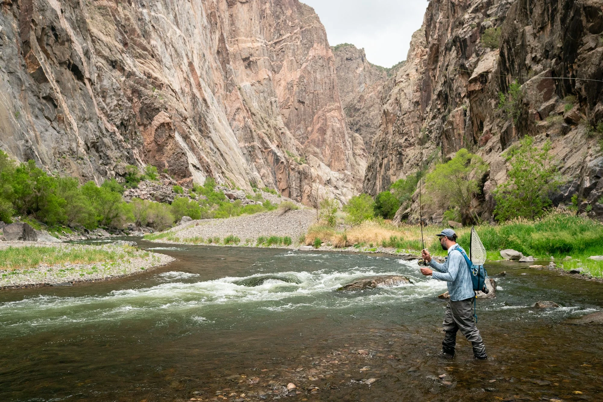 An angler fishes shallow current beneath towering canyon walls in the Black Canyon