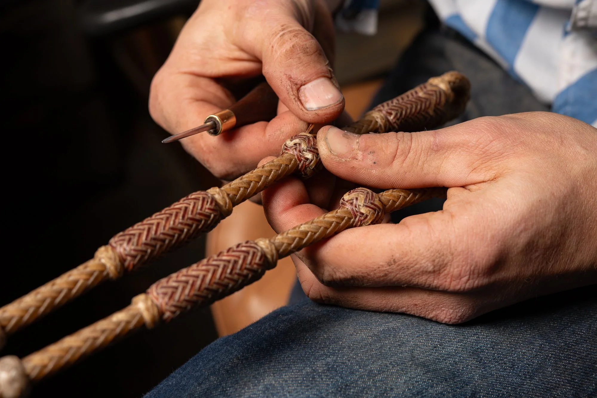 Hands tying a decorative knot on a braided rawhide romal rein using a traditional braiding fid