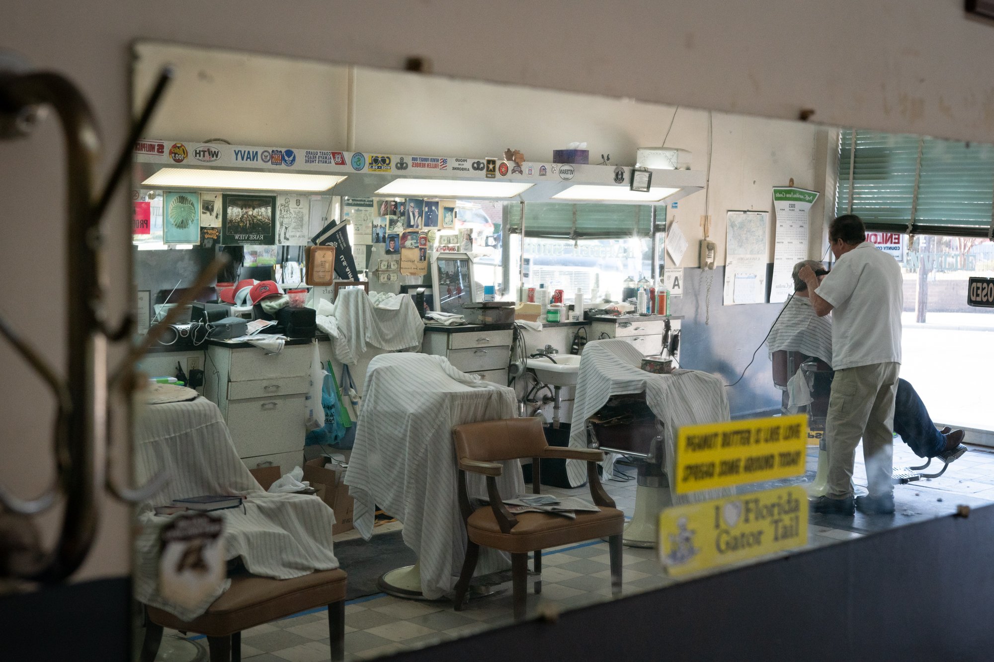 Interior view of a traditional barbershop with barber chairs, mirrors, and military flags on the wall
