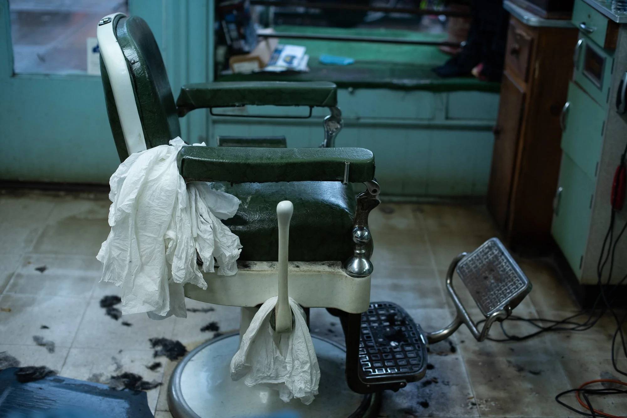 An antique barber chair with white rags hanging from the armrest at a traditional barbershop in Brooklyn, NY