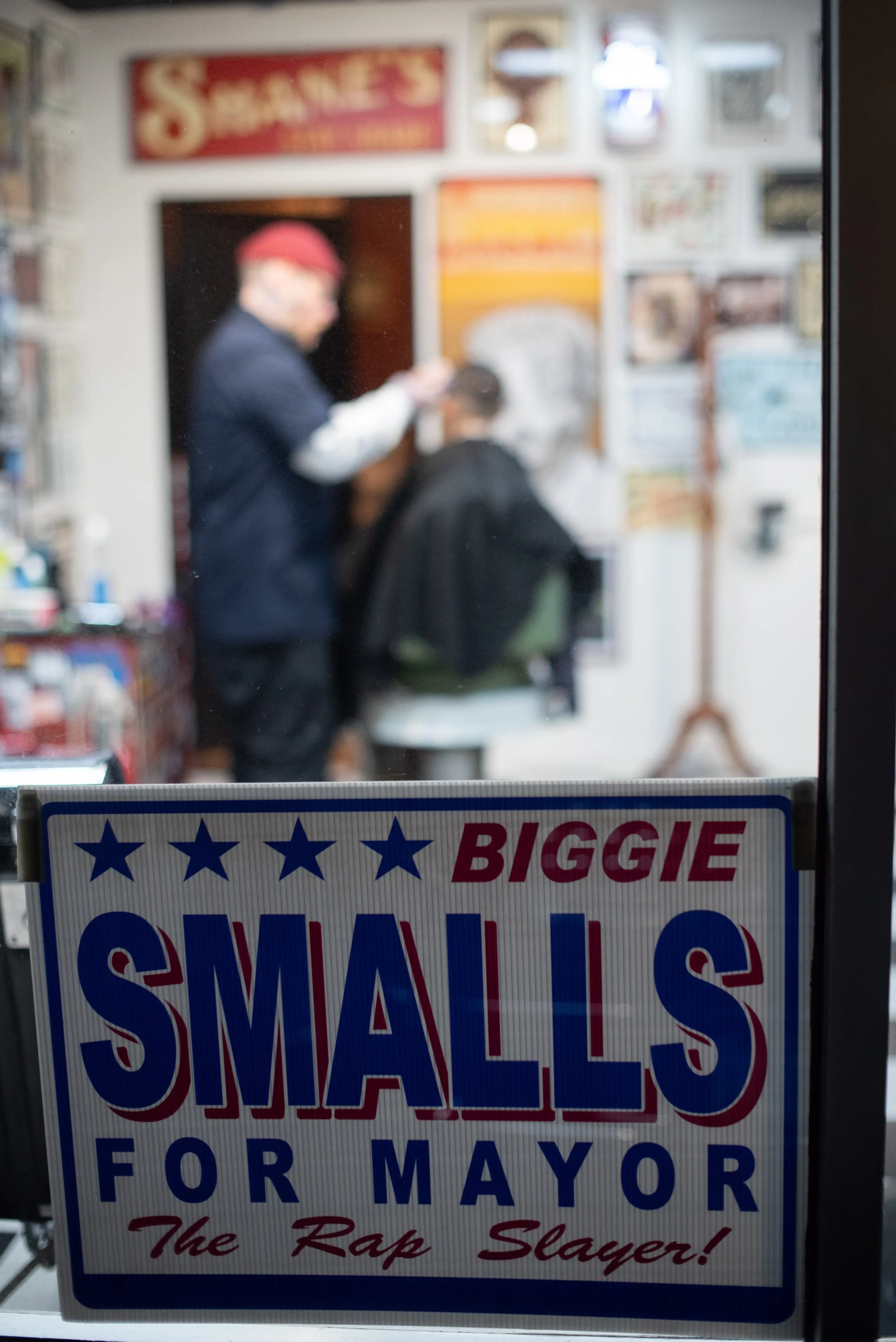 view through window into Shane's Barbershop San Mateo with barber cutting hair and campaign sign in foreground