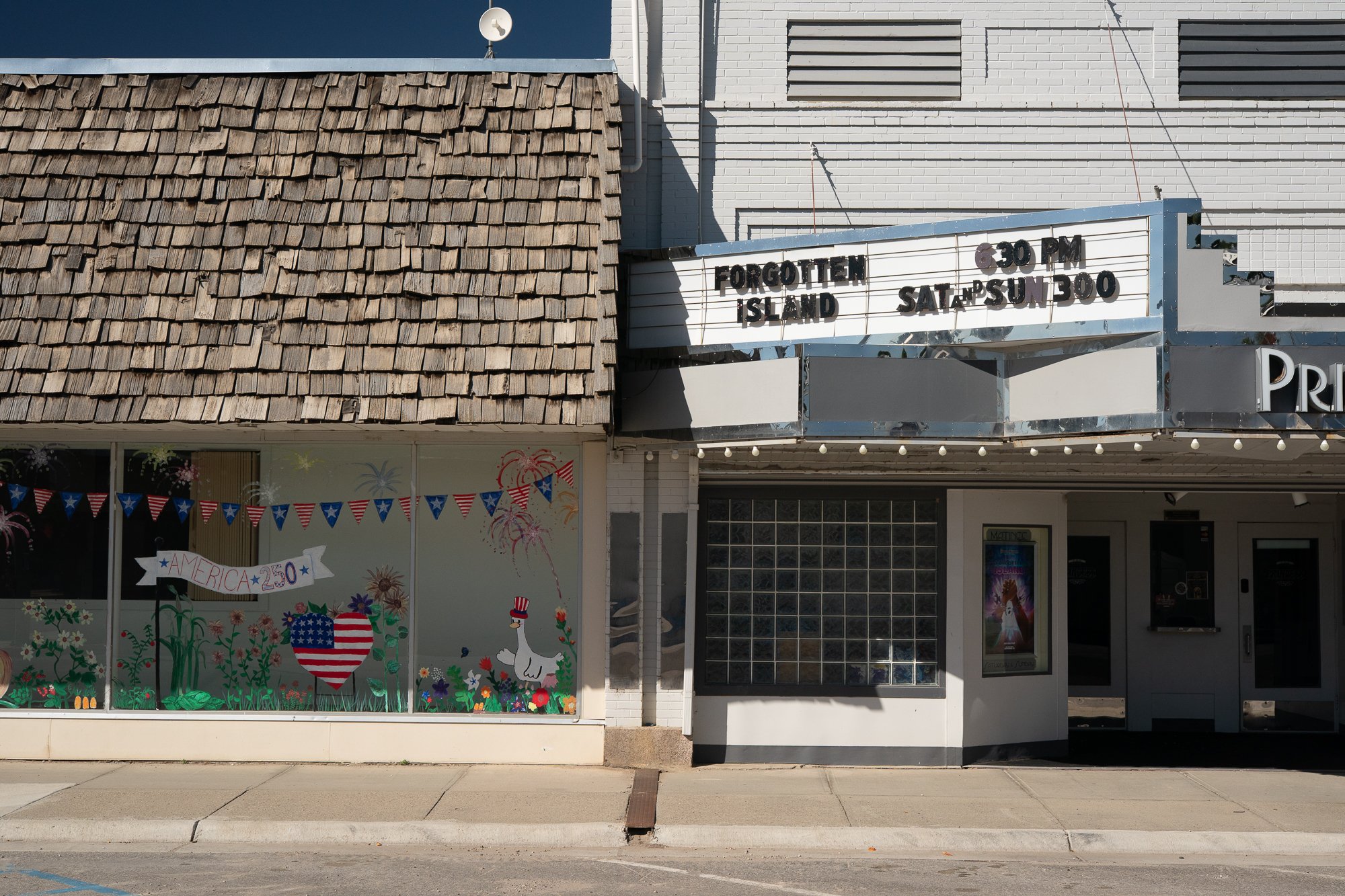 Princess Theatre exterior in downtown Douglas, Wyoming, with a movie marquee, glass block windows and a neighboring storefront decorated with American flags.