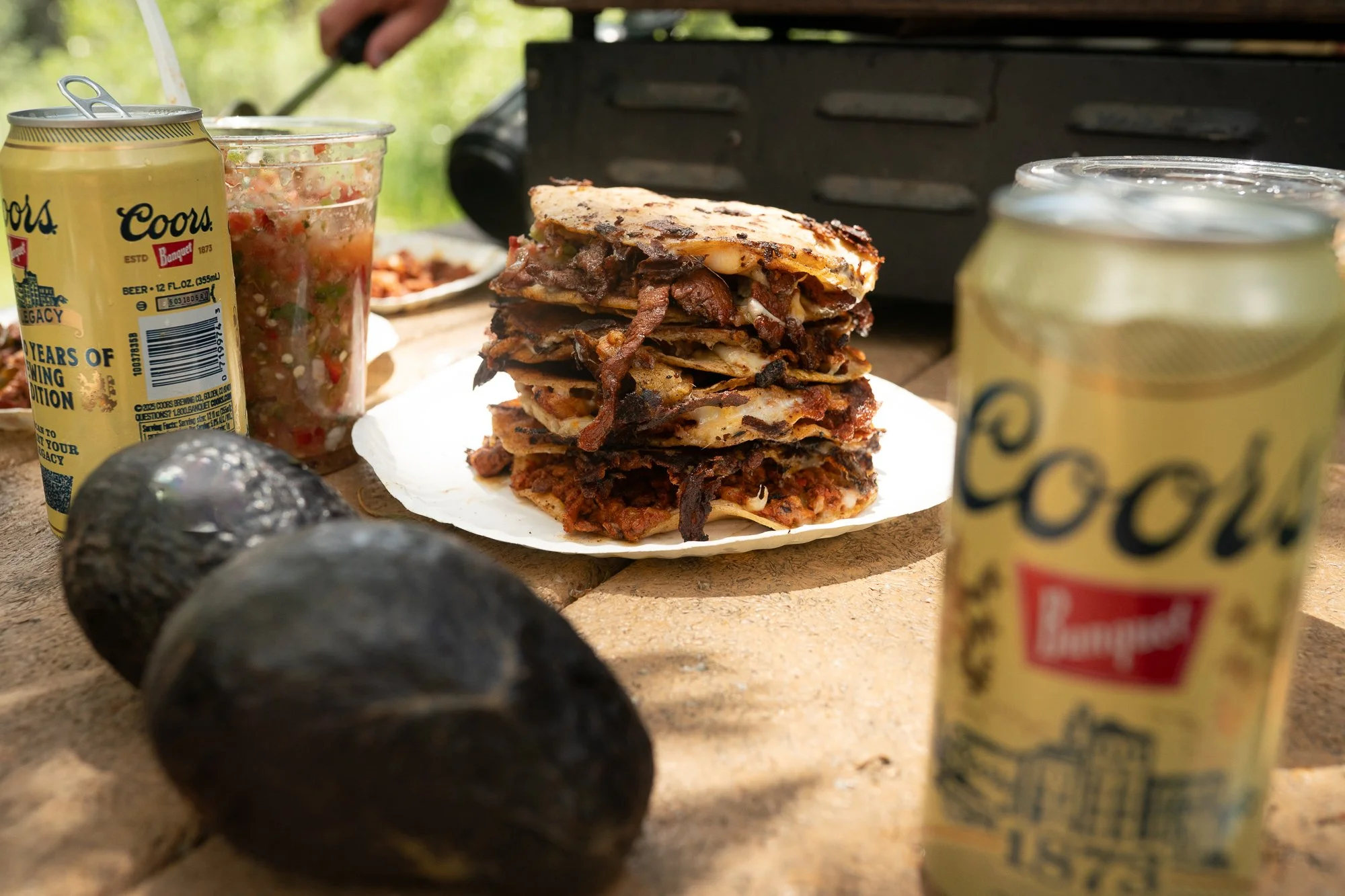 A stack of tacos, salsa, avocados, and drinks sits on a table during a riverside break from a Duck Camp fly fishing shoot
