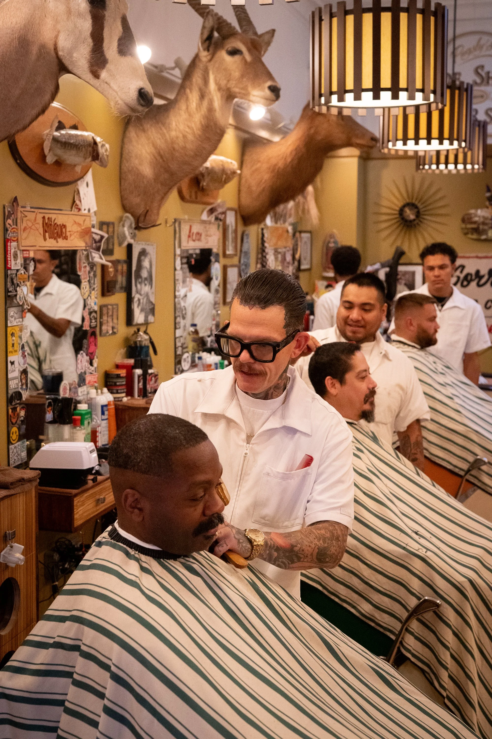 Barbers in white uniforms trim clients’ hair inside Pugsly’s Barbershop.