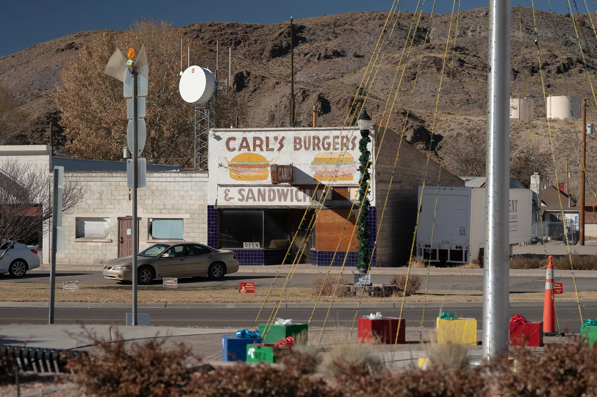 Carl's Burgers and Sandwich shop with a hand-painted facade sign in a small Nevada town, colorful Christmas decorations in the foreground and a desert hill behind the building.