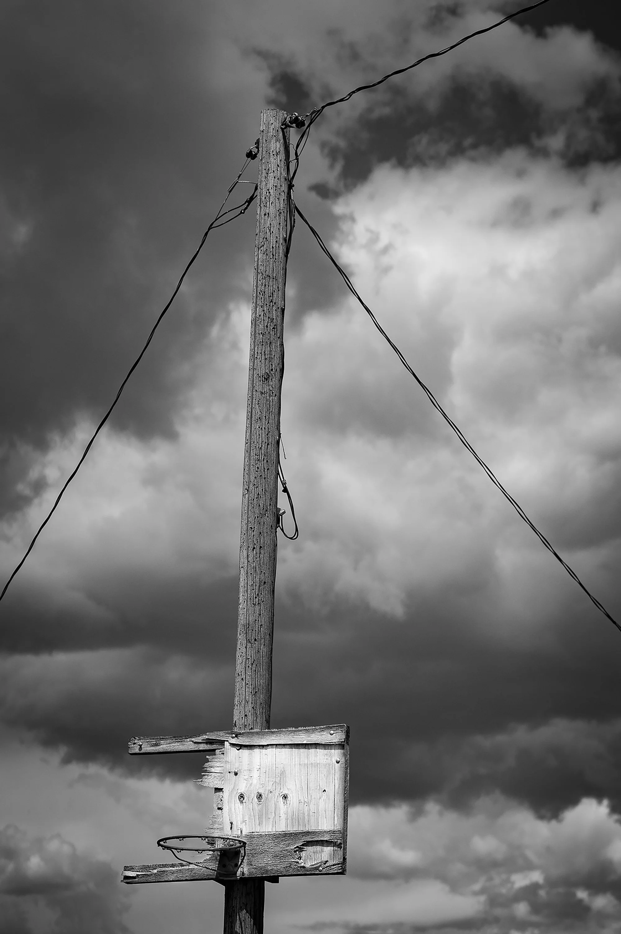 Weathered basketball hoop and wooden utility pole beneath dark storm clouds