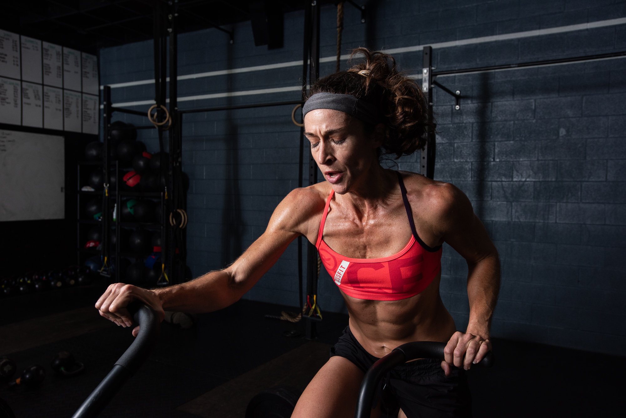 Female athlete using air bike in crossfit gym during high intensity conditioning workout photoshoot