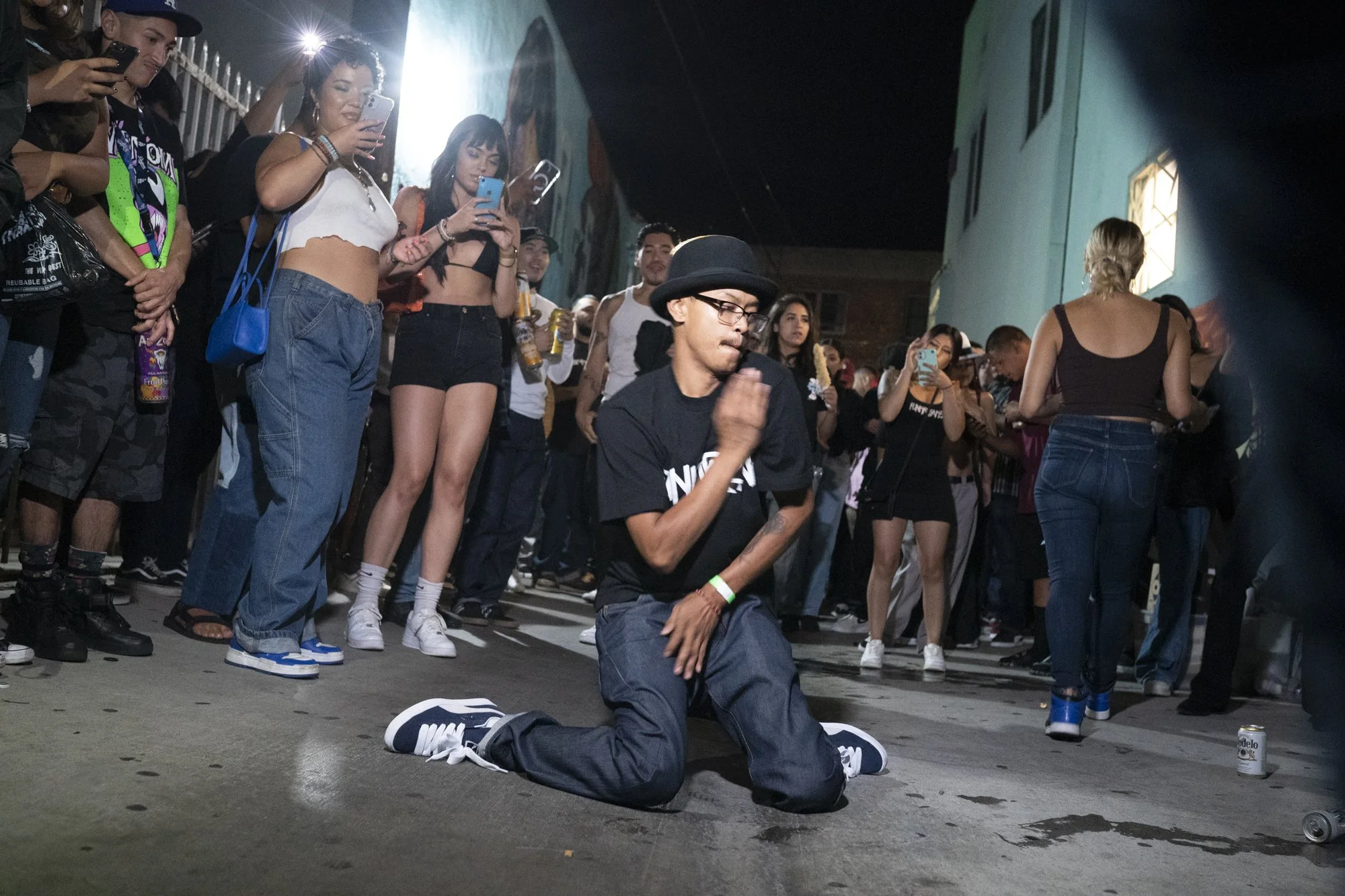 Dancer in a bowler hat performing on one knee in the center of a crowd circle in the alley behind Syndicate Barbershop in Long Beach during the 20th anniversary party