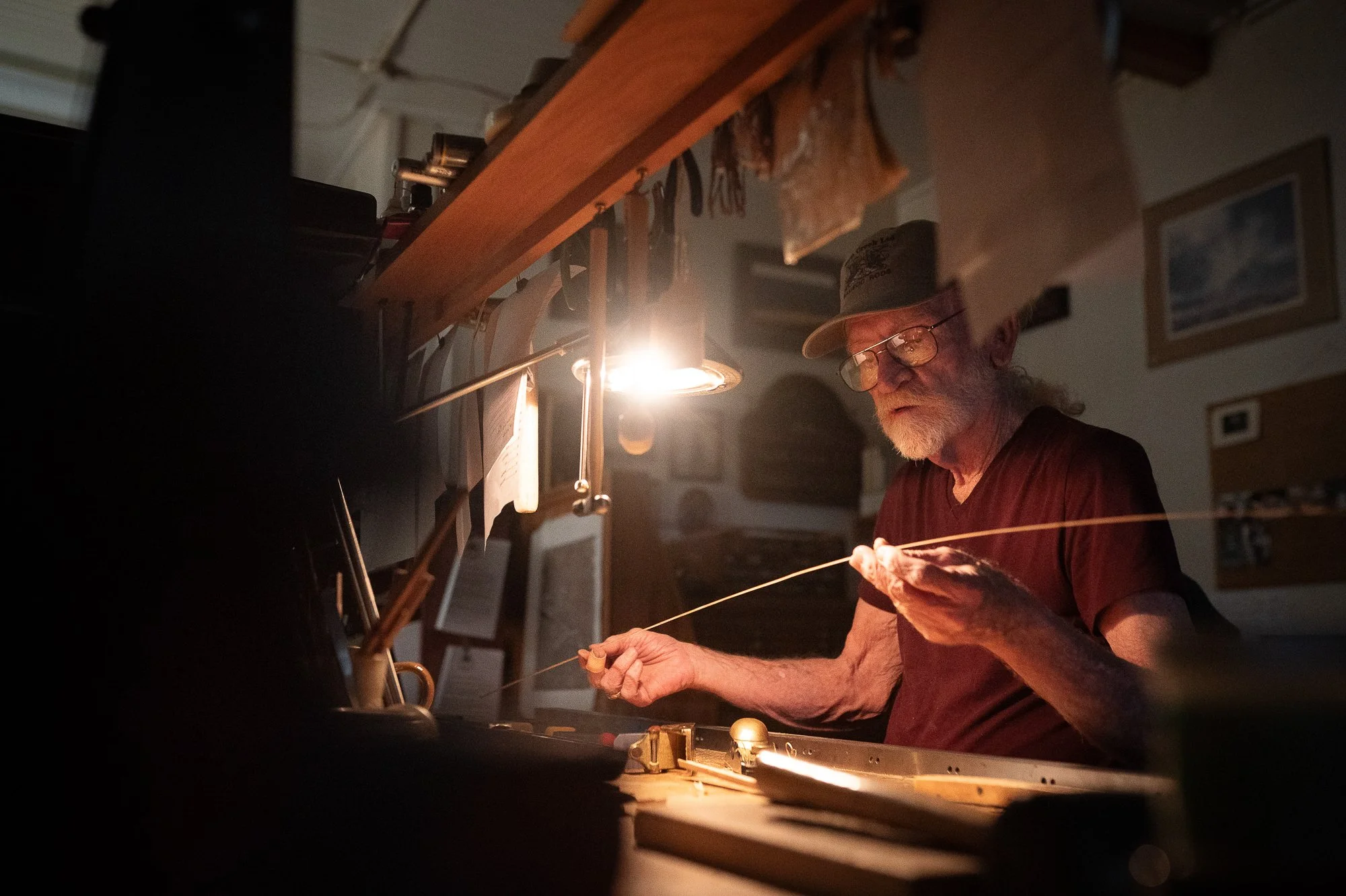 Mike Clark inspecting a long strip of bamboo cane while building a fly rod at his workbench.