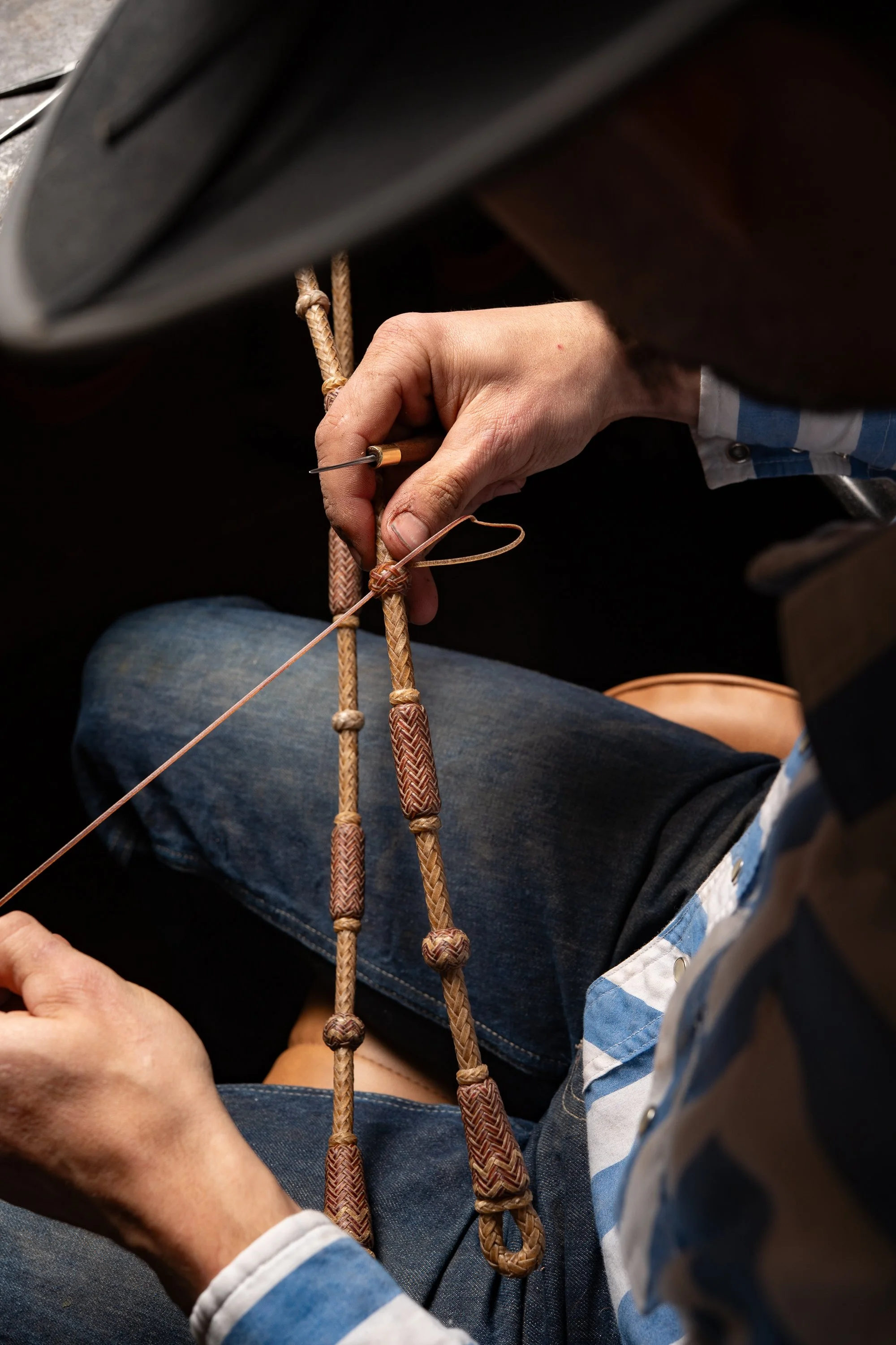 Dakota May tying a decorative knot on a braided rawhide piece while working at his bench