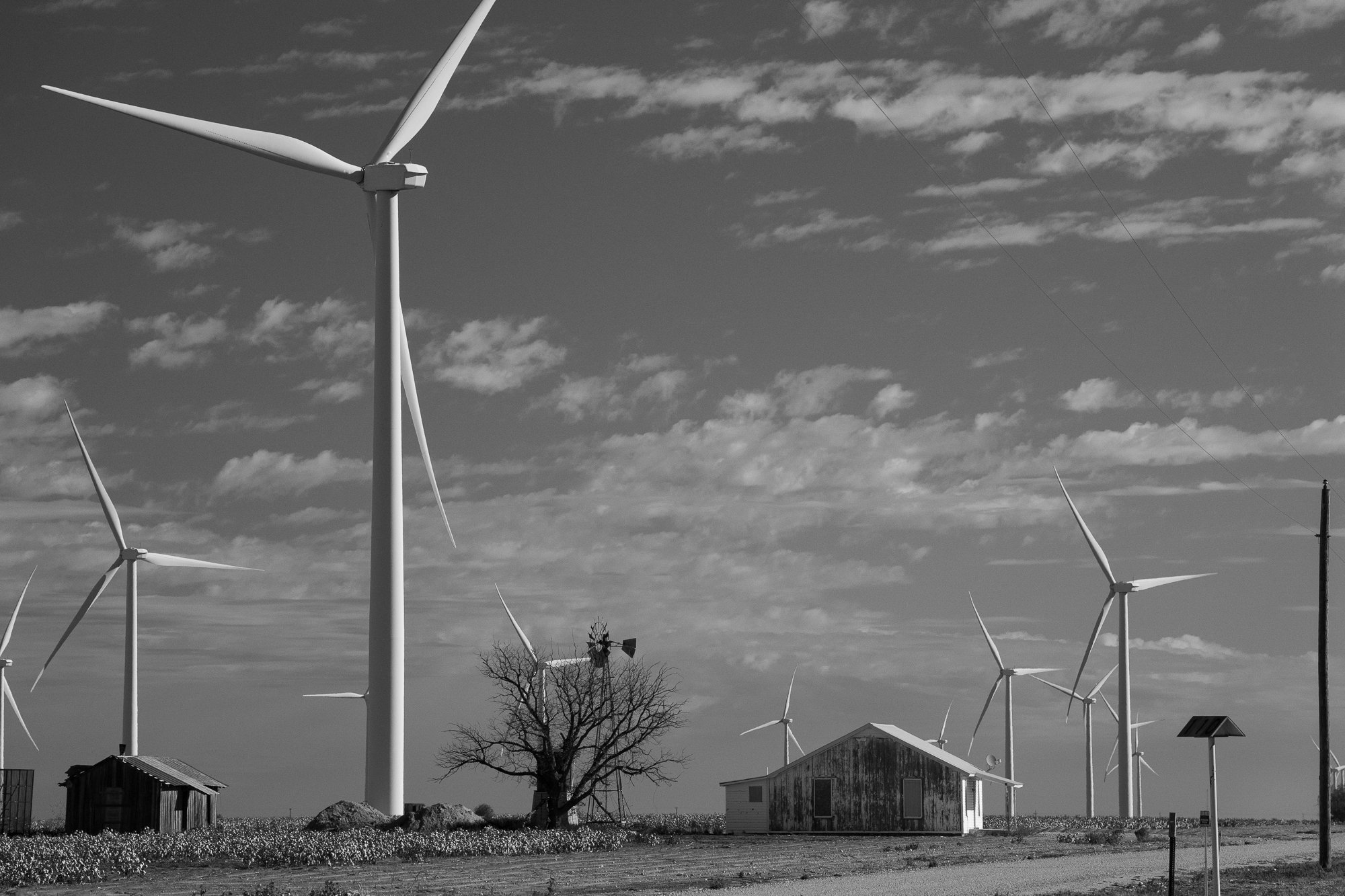 Wind turbines towering over abandoned rural buildings on the Llano Estacado in Texas