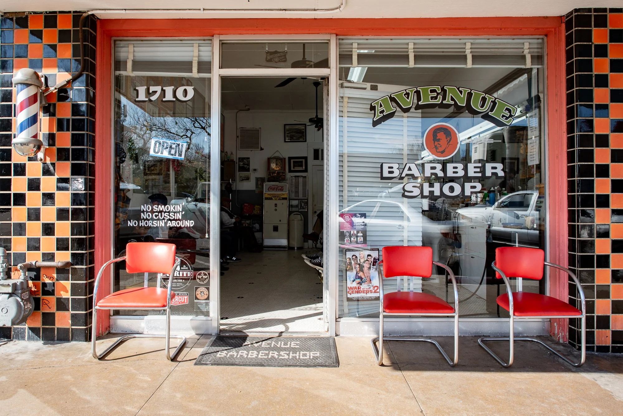 Exterior storefront of Avenue Barbershop in Austin Texas with vintage signage and red chairs outside on South Congress