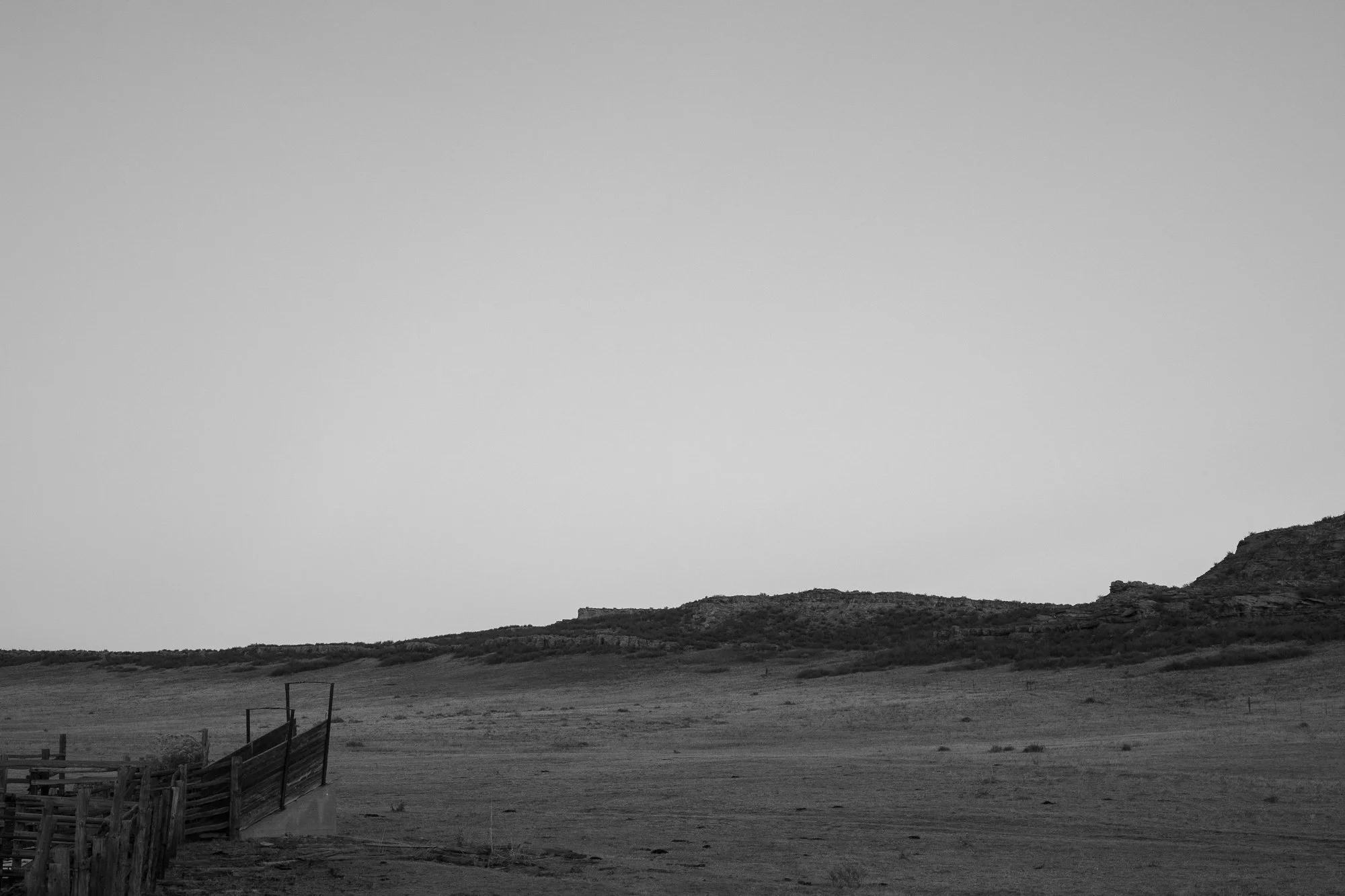 Black and white photograph of a corral set within an open Western landscape