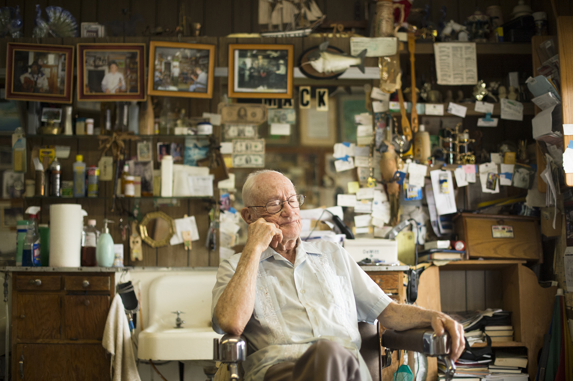  Portrait of an old barber sitting in his chair at a traditional barbershop filled with junk  