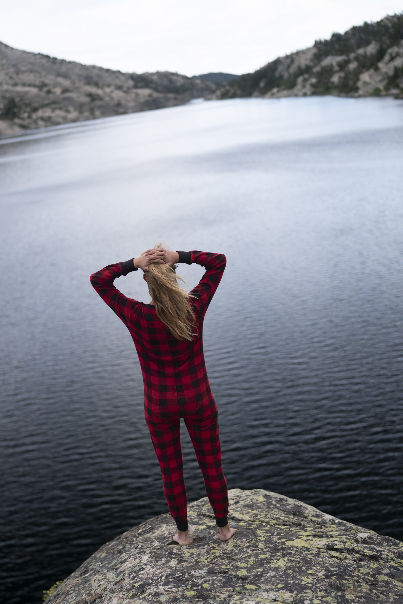  A girl in red and black pajamas standing on a rover overlooking Seneca Lake in the Wind River Range - Wyoming.  