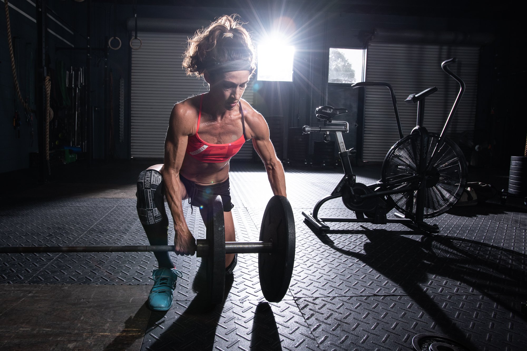 Female athlete lifting barbell from floor in gym during strength training photoshoot