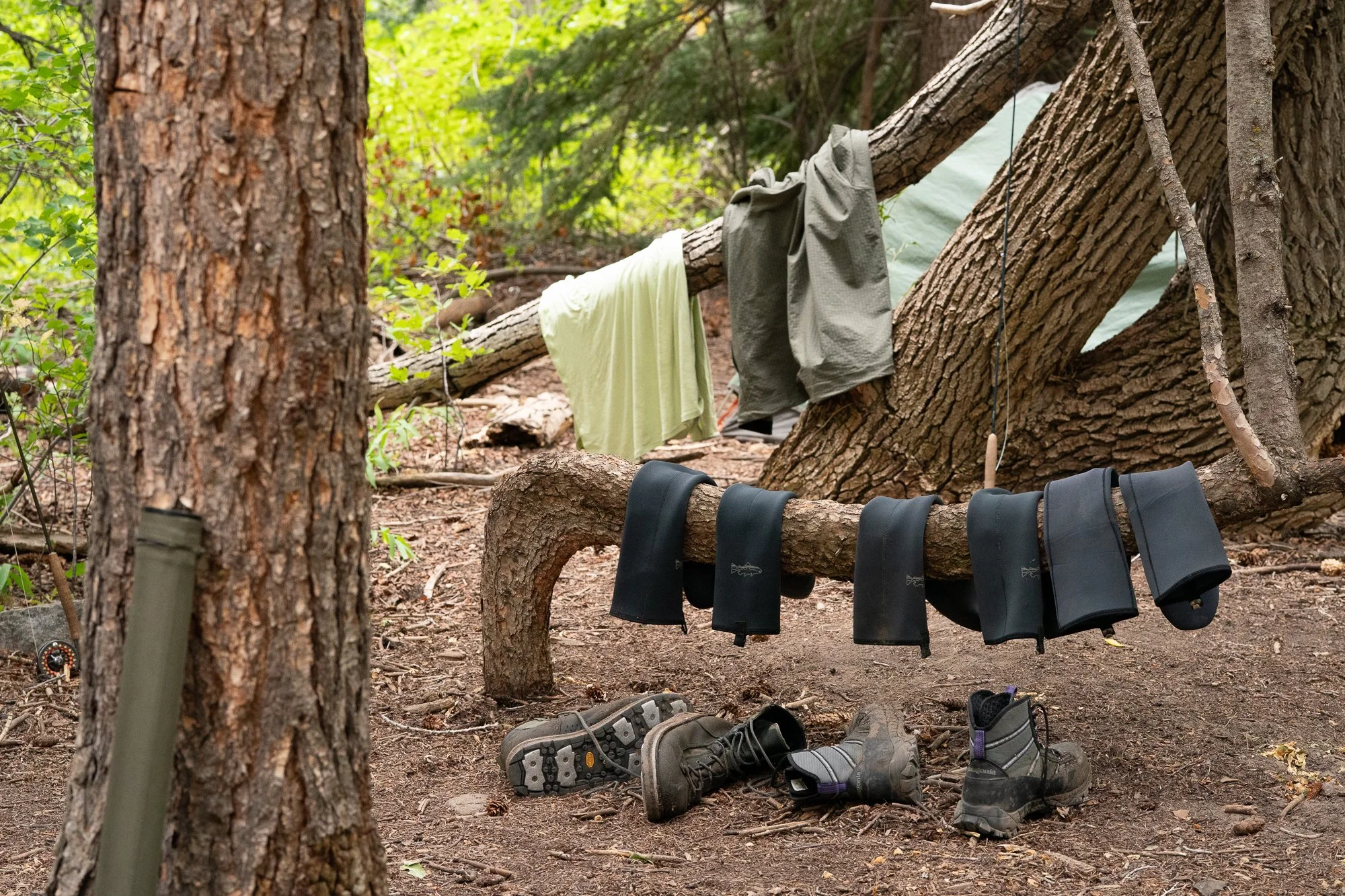 Fly fishing boots, neoprene socks, rods, and clothing hang around a riverside camp
