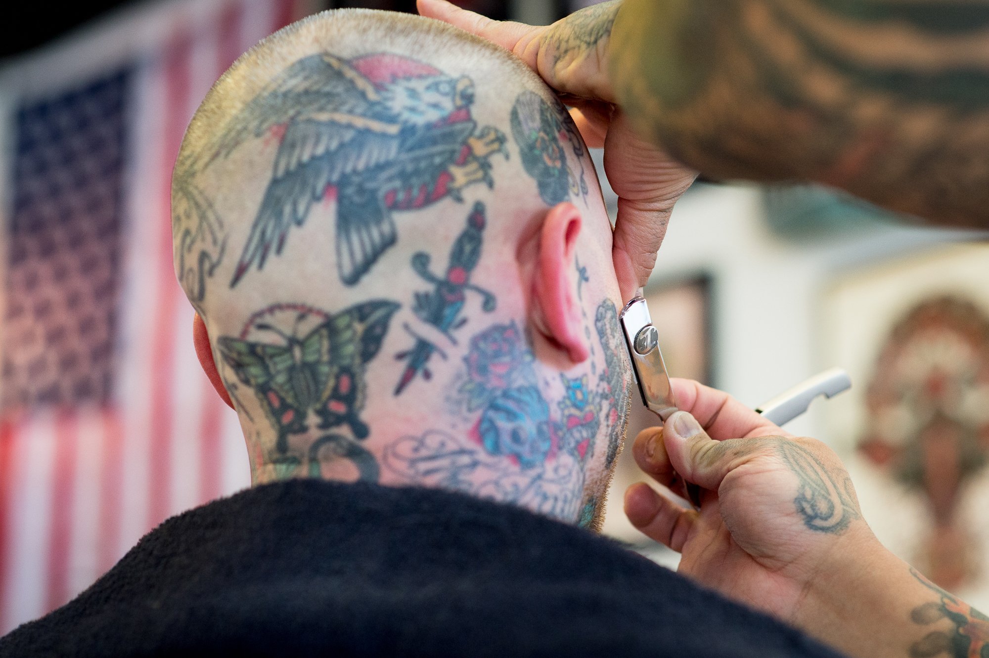  Photograph of a person with a completely tattooed head getting shaved at a barbershop  