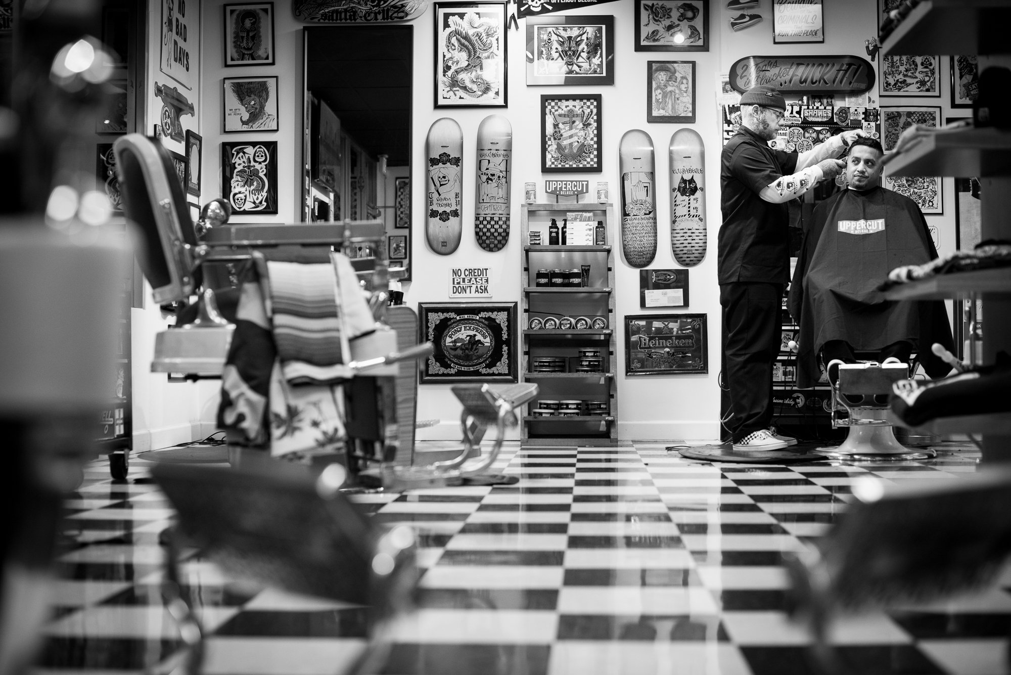 Black and white photograph of a barbershop with skateboards covering the walls - Shane’s Barbershop - San Mate, CA 
