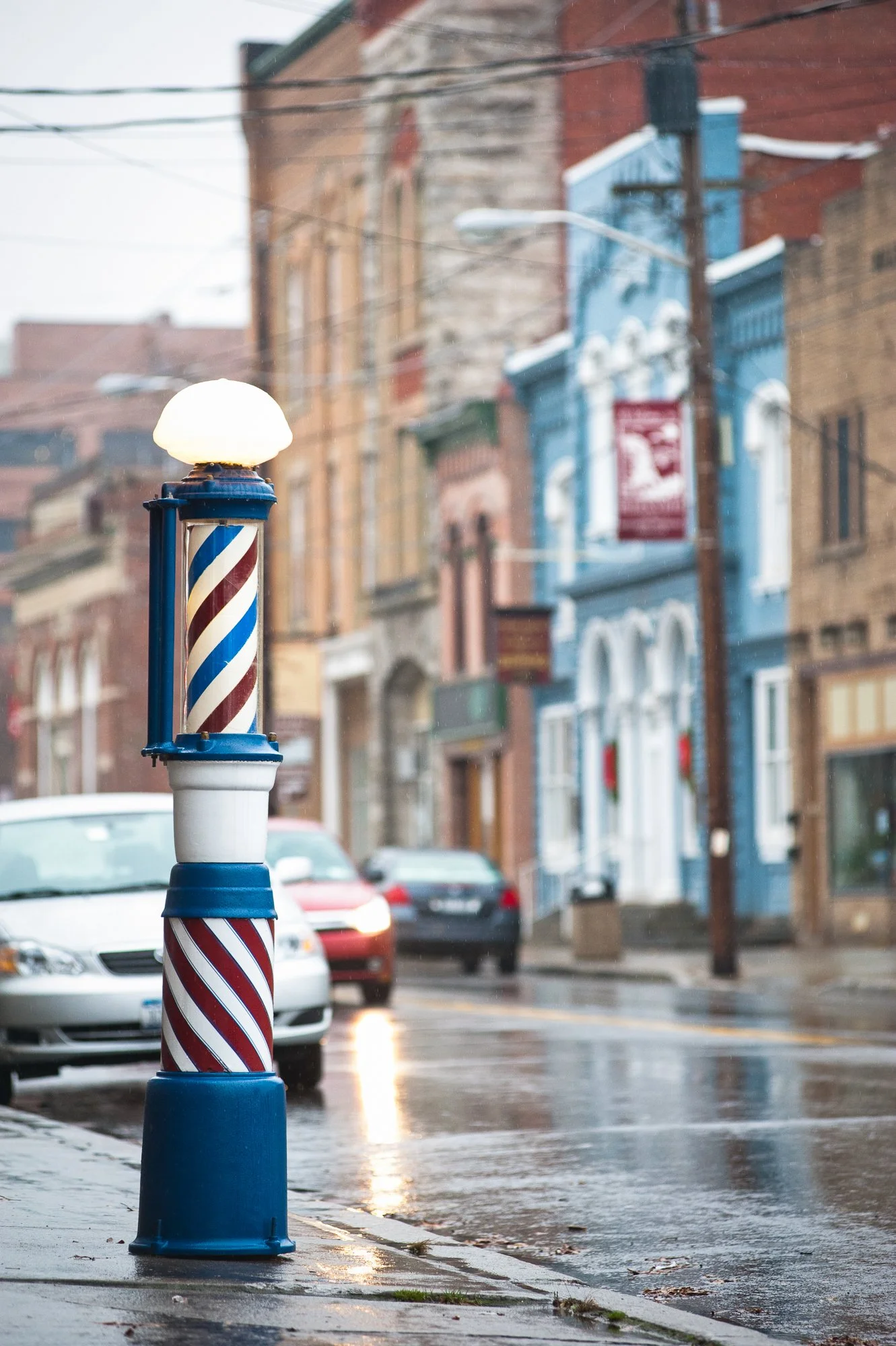  Photograph of an old antique barber pole on the sidewalk in front of a tradition barbershop in a small American town.  