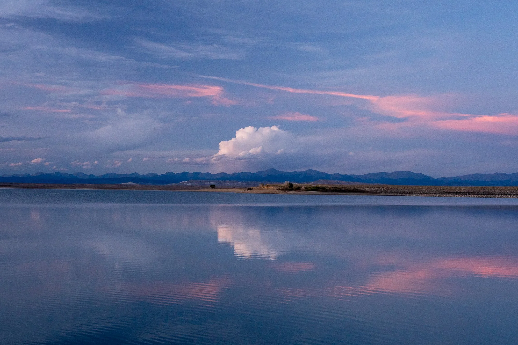  Still water reflects a pastel evening sky as distant land forms dissolve into soft color. The photograph emphasizes balance, reflection, and the meditative qualities of open space. 