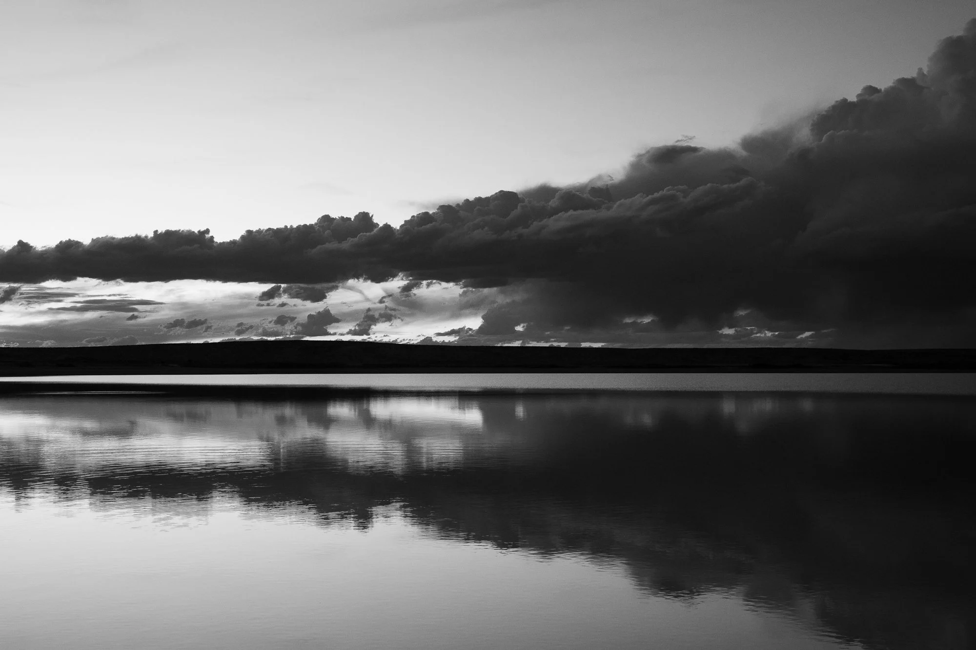  Towering clouds gather in layered formations, illuminated by fading light that shifts between pink and blue. The image captures quiet tension and the vastness of the atmosphere. 
