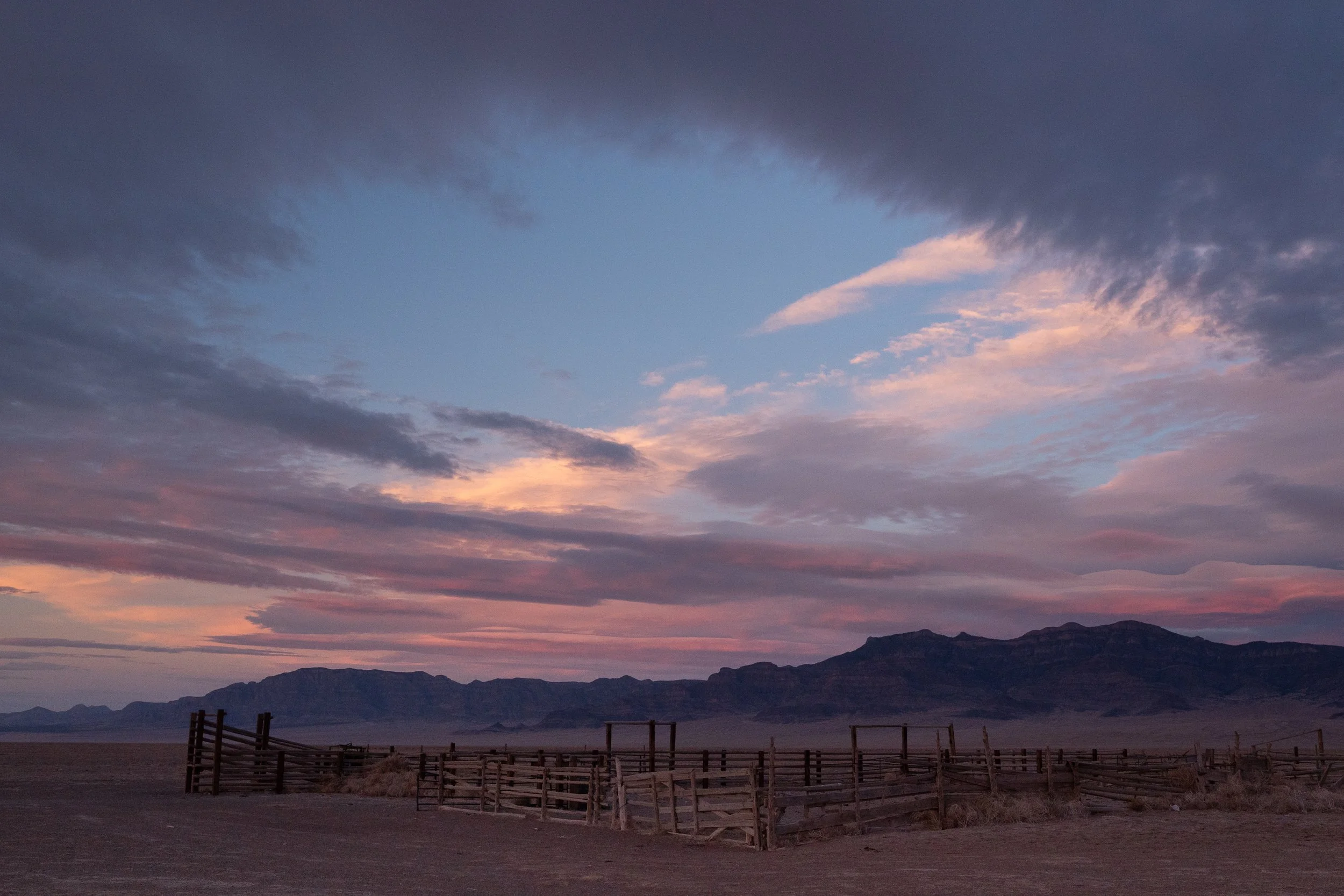  Expansive corral system in an open desert landscape beneath soft pastel sunset clouds. 