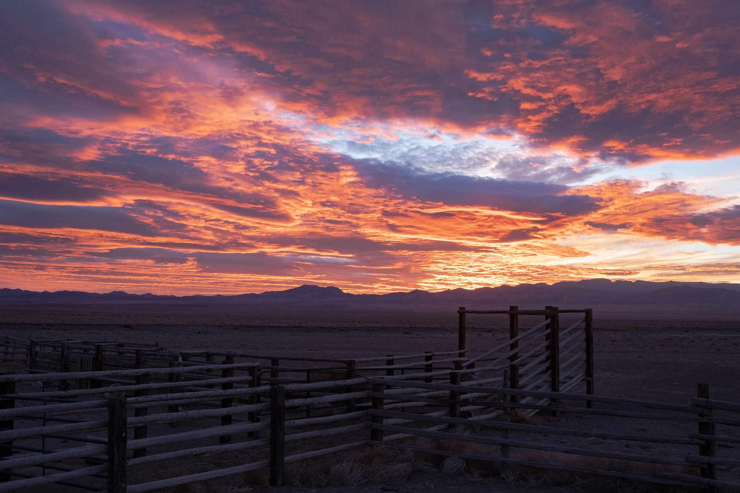  Wooden corral fencing stretching across the foreground under a vivid and dramatic sunset sky. 