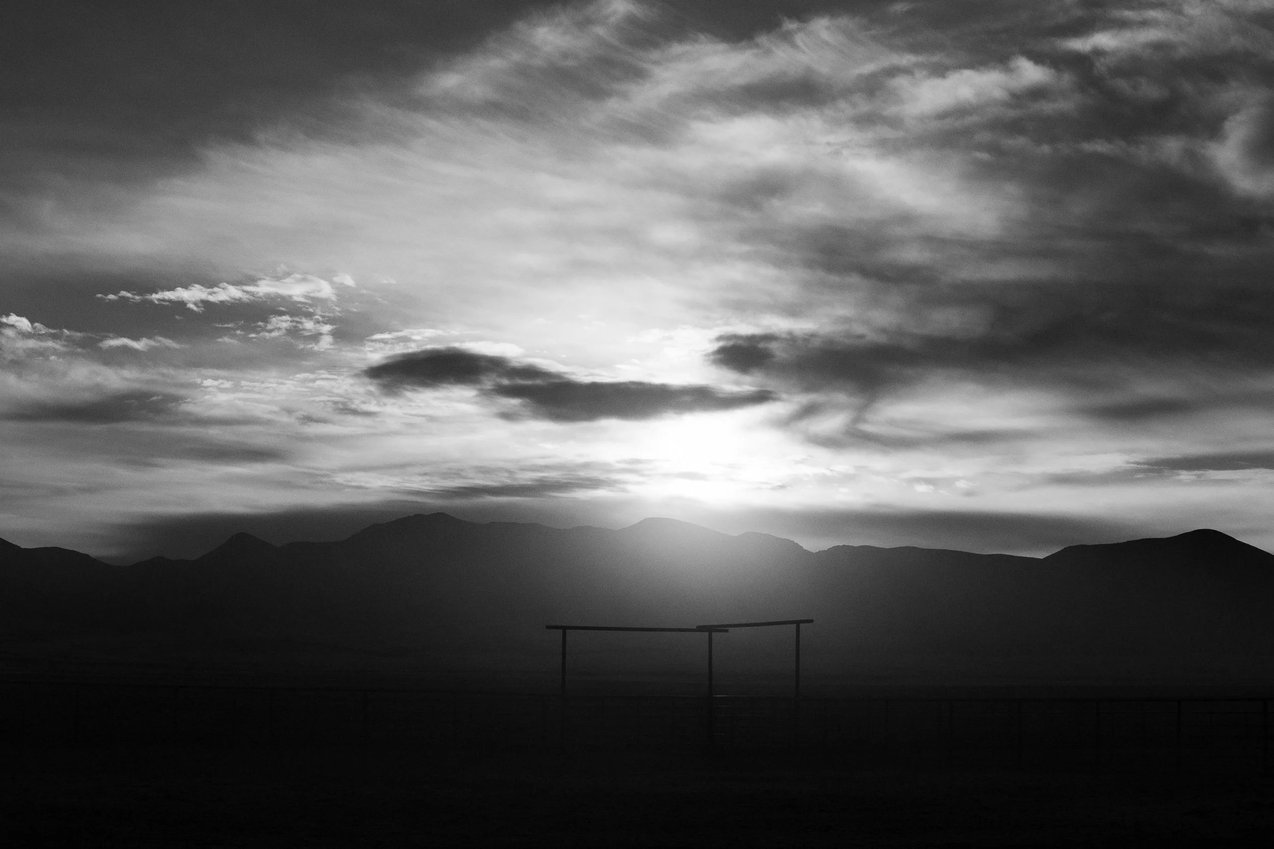  Silhouetted corral gate against bright rising light with mountains fading into the background. 