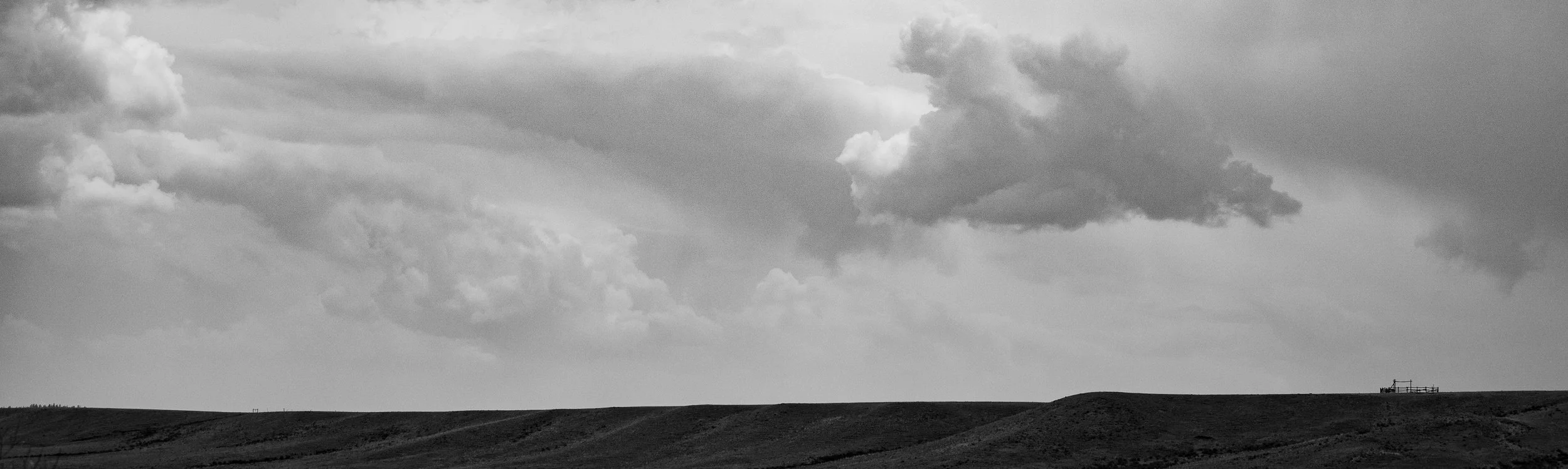 Long minimalist landscape with a distant corral structure barely visible along a rolling horizon line.