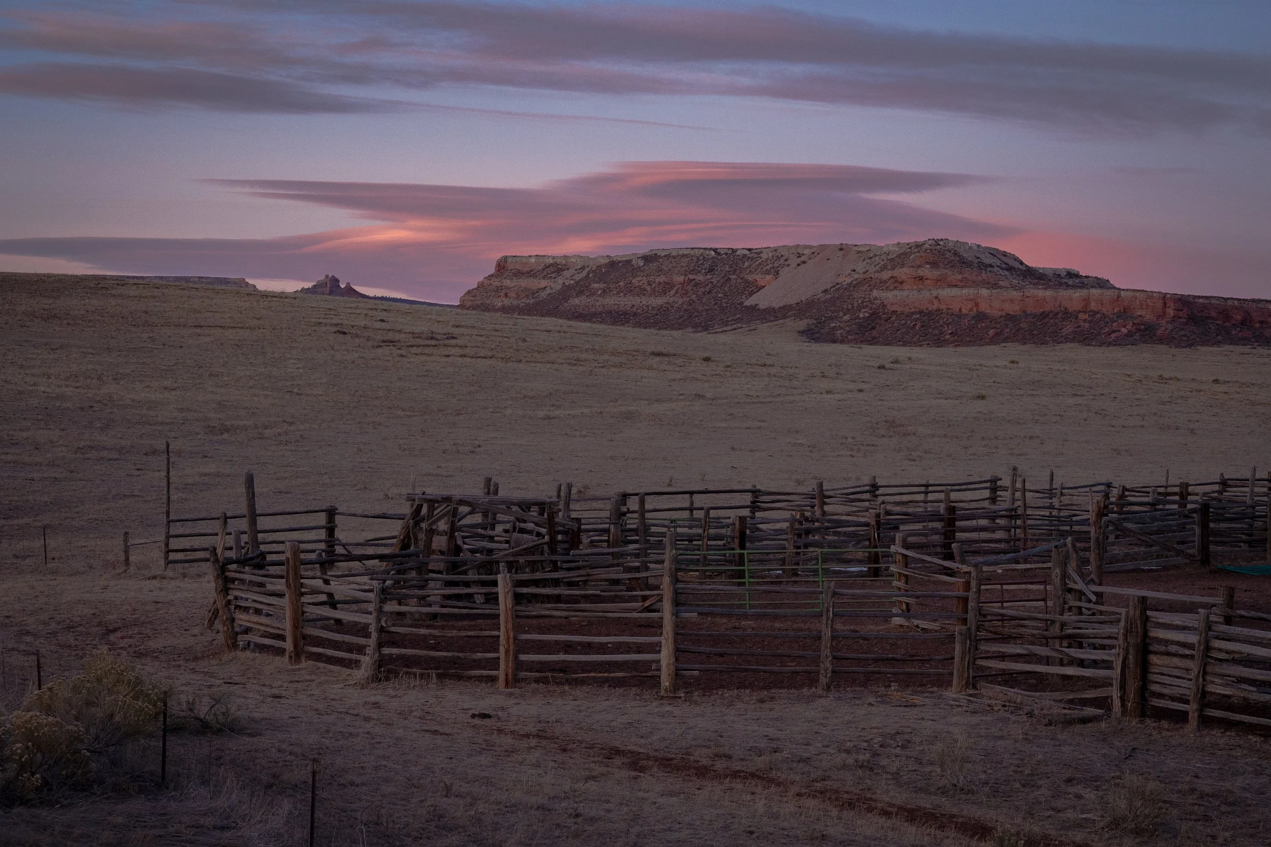  Wooden corral enclosure set against desert cliffs glowing with soft pink sunset light. 