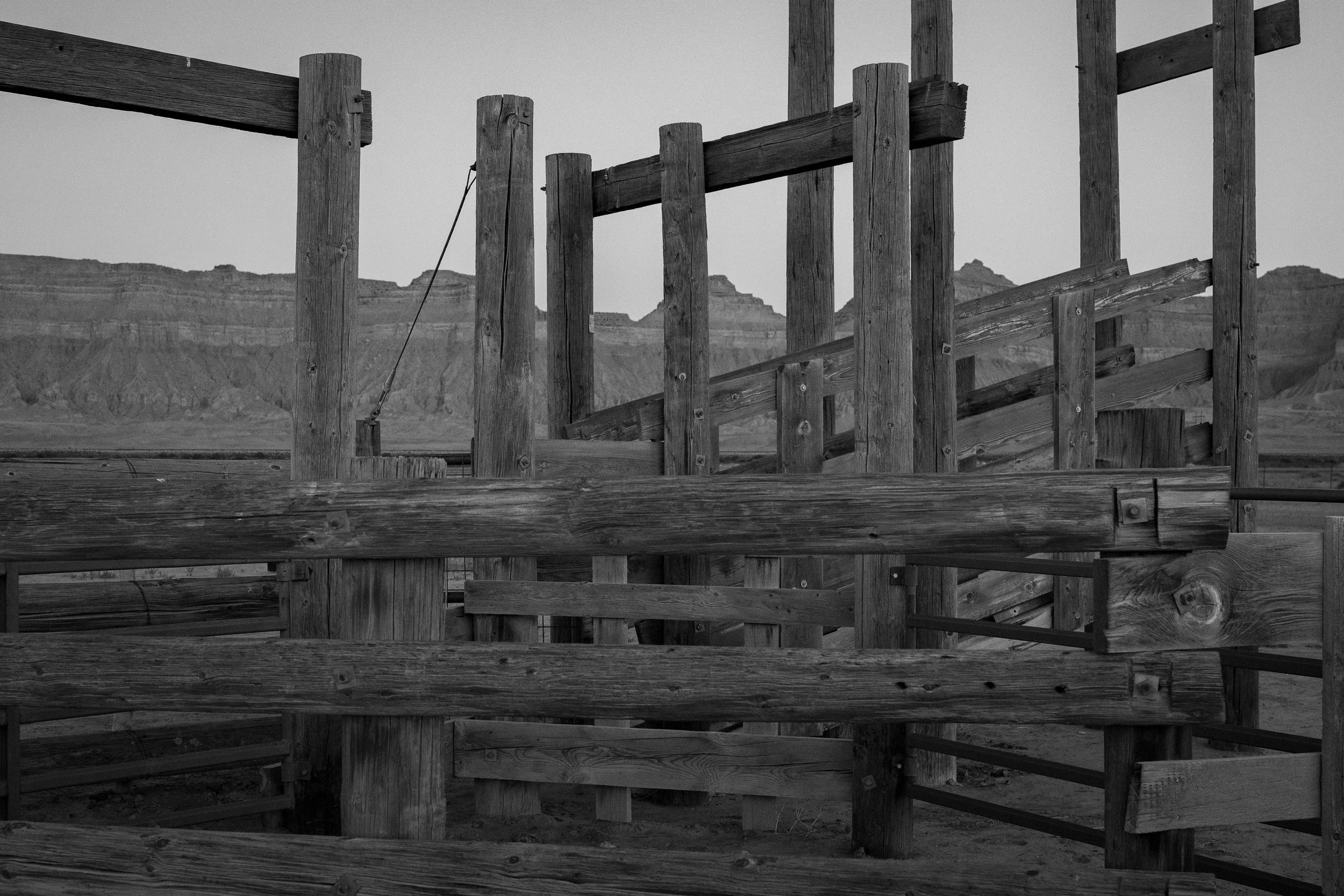  Ranch chute and fencing structure framed by desert badlands and open sky in muted tones. 