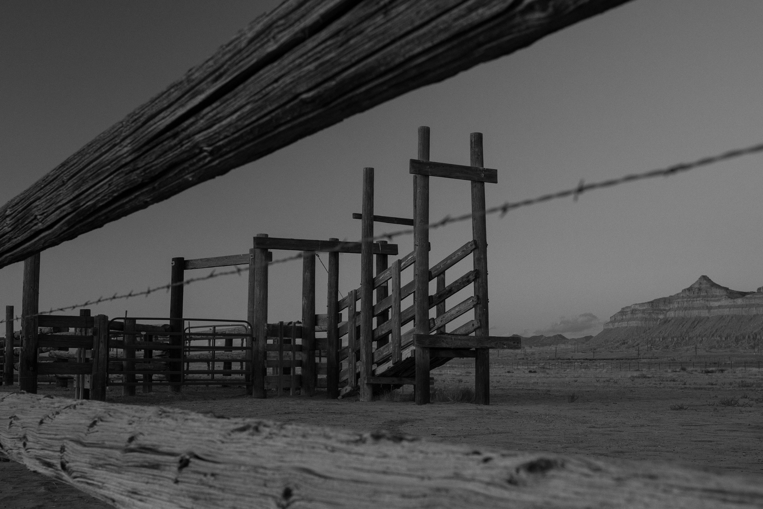  Low angle view of a wooden loading chute and fencing set within a vast open desert landscape. 