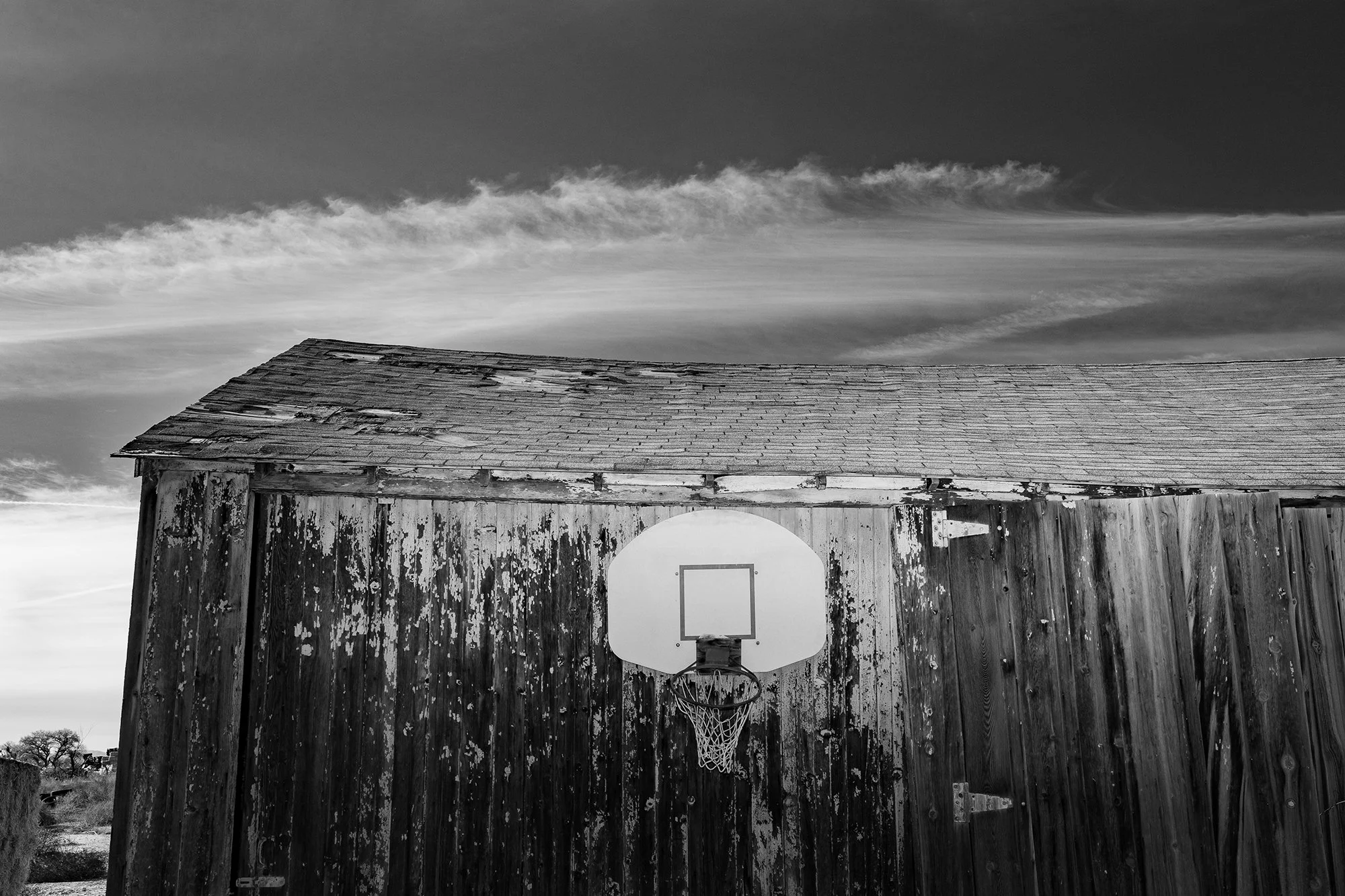  Black and white photograph of a basketball hoop on an old wood barn with dramatic clouds behind it in Nevada  