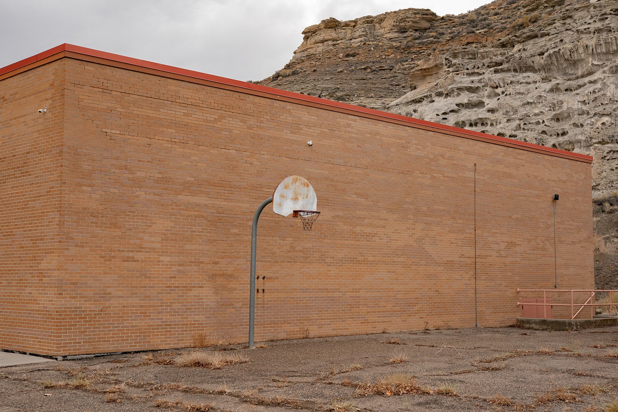  Photograph of a basketball hoop outside an old brick gymnasium at an abandoned school in America  