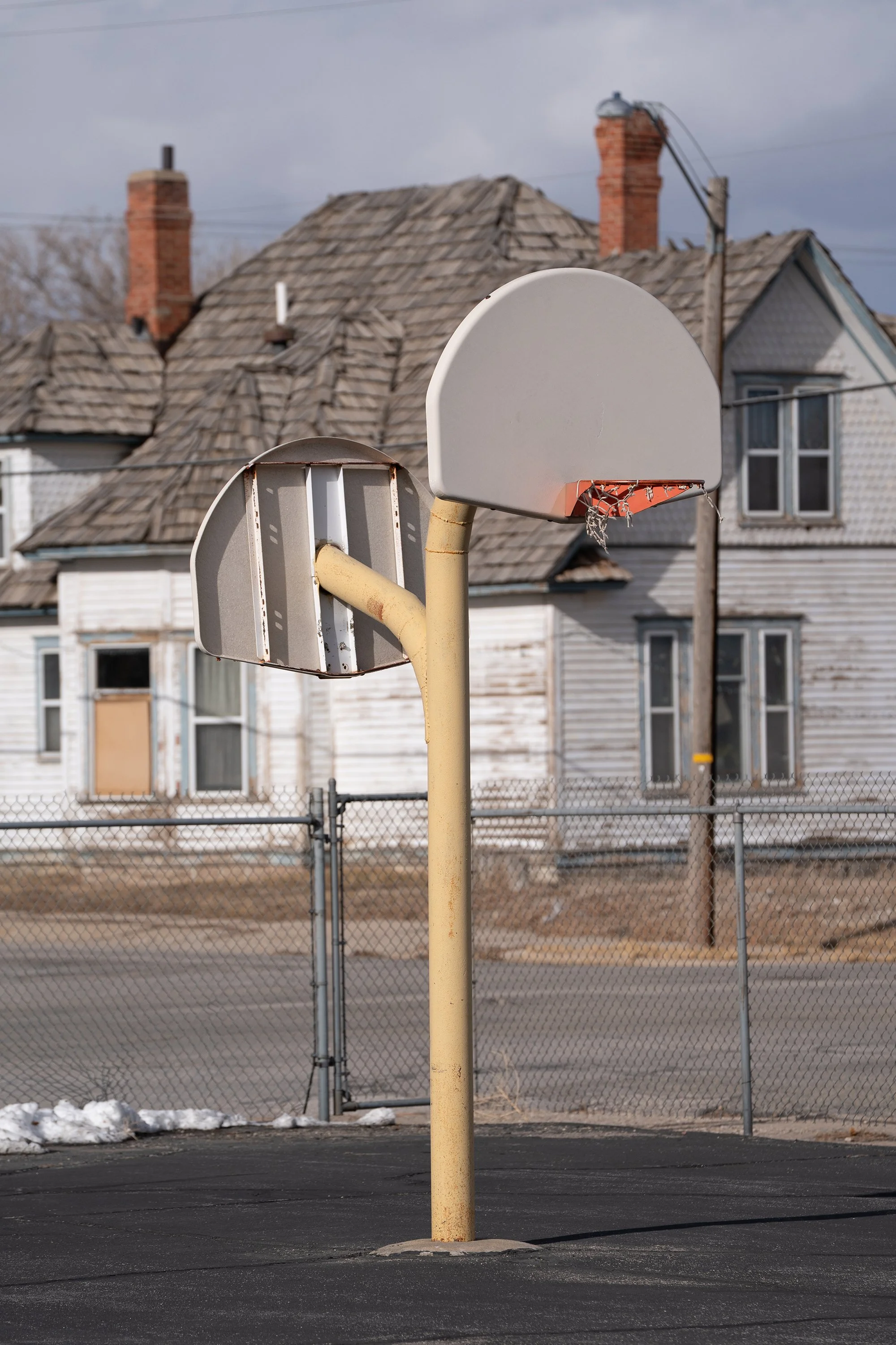  Photograph of a basketball hoop in front of an old house with a unique wood shingled roof in a small town in the American West.  