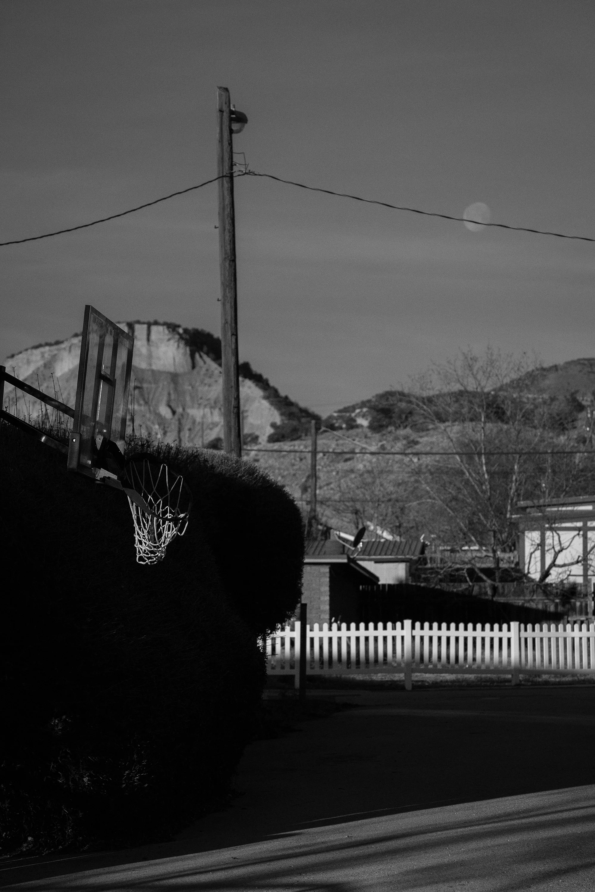  Photograph of a basketball hoop early in the morning in a small Wyoming town with the moon still in the sky  