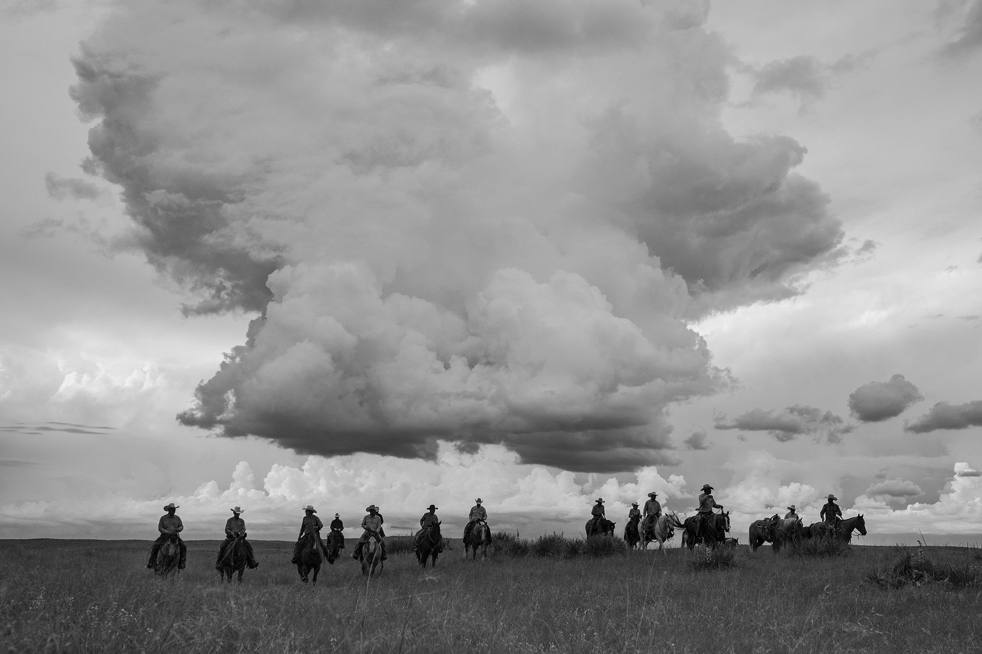  Authentic black and white photograph of cowboy riding across open range under a large storm cloud  