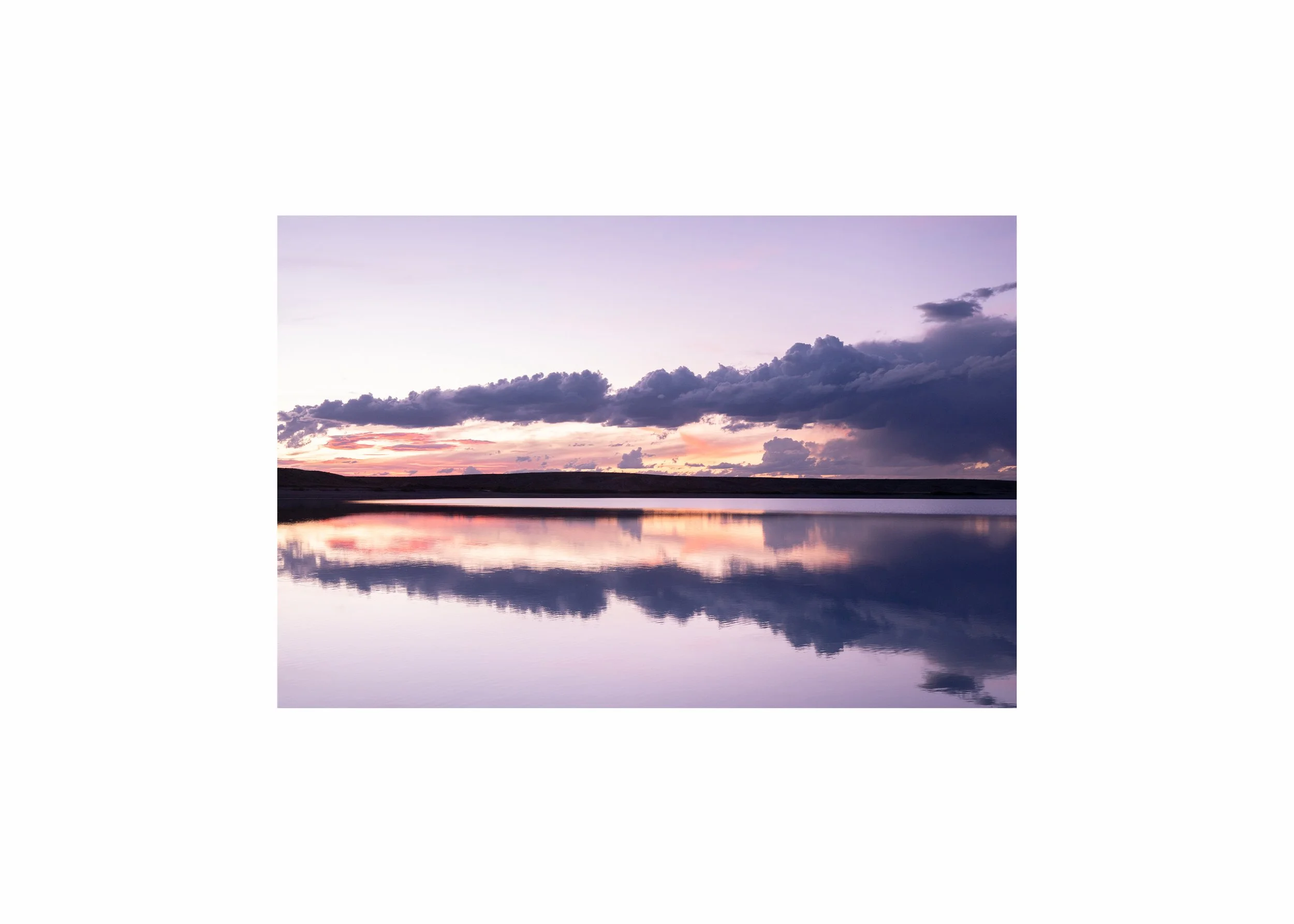 A calm lake reflecting a pink and purple sunset with dark clouds.