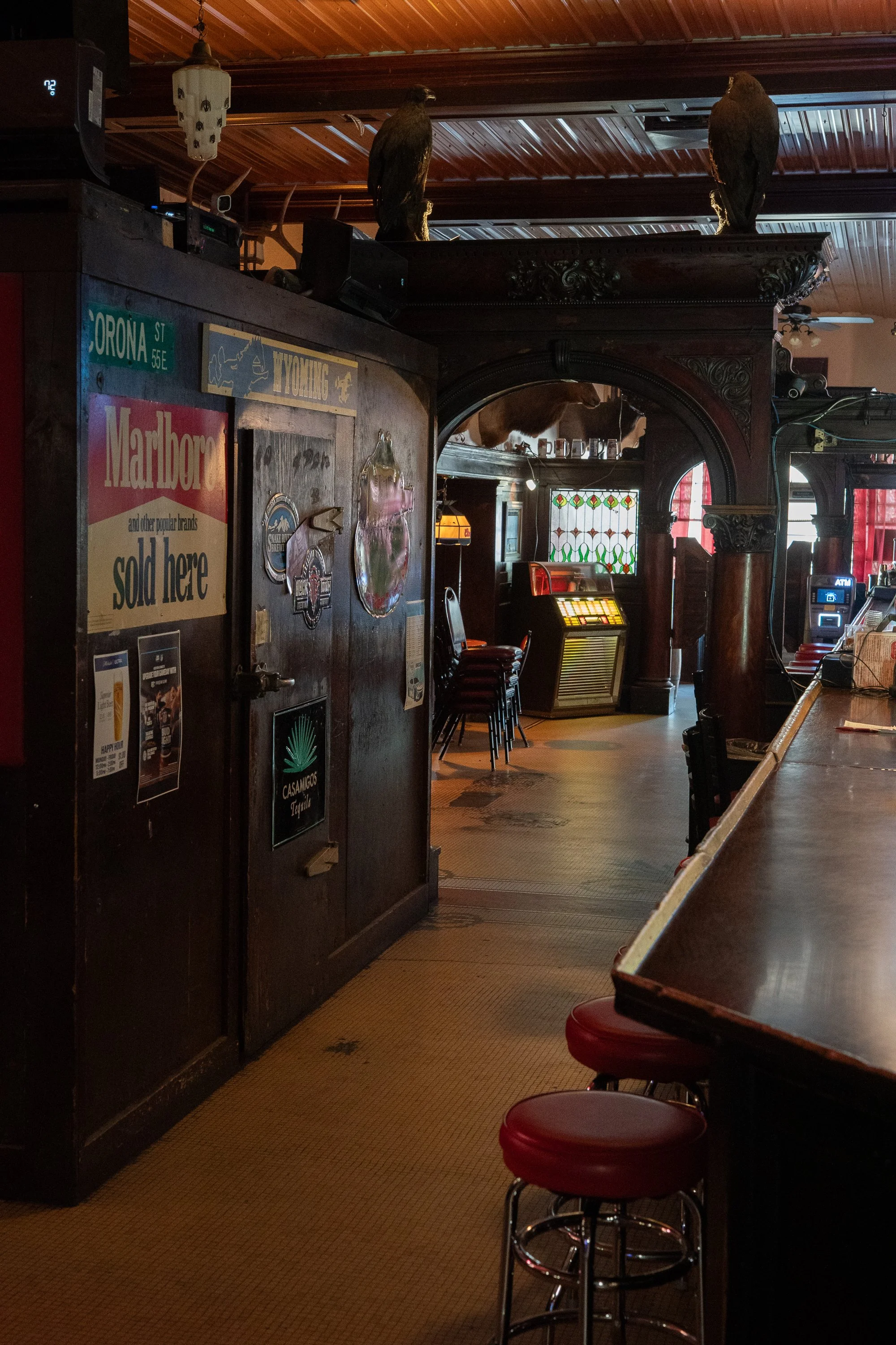 Interior of the College Inn in Douglas, Wyoming, with a long wooden bar, red stools, vintage signs, an ornate wooden arch and mounted birds.